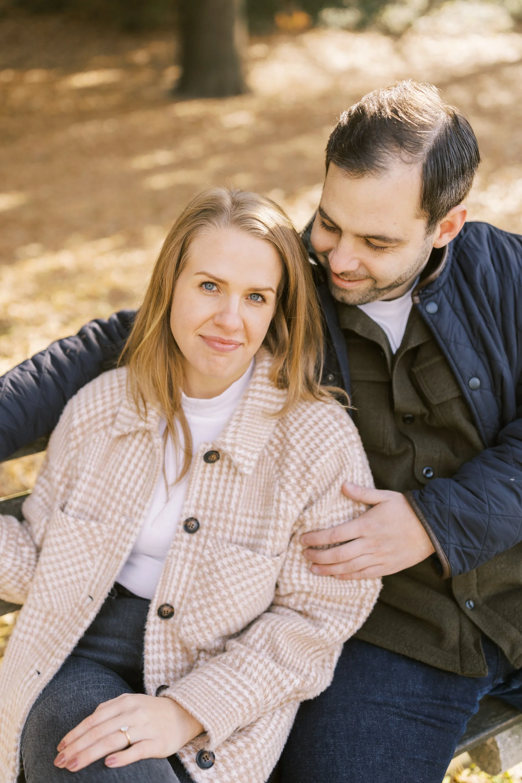 A couple sitting on a bench in a park as one leans into the other 