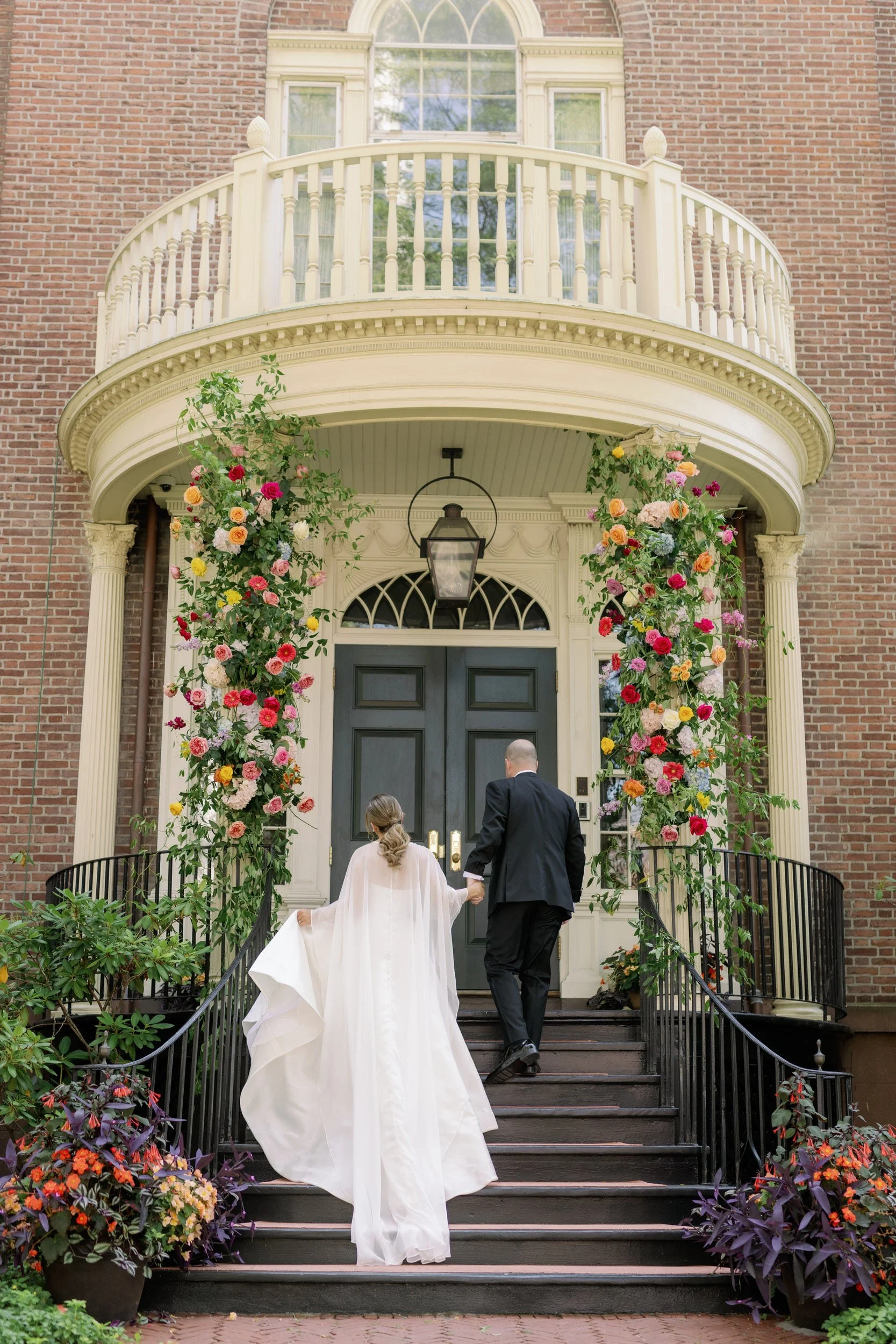 Newlyweds holding hands and walking into a red brick house 