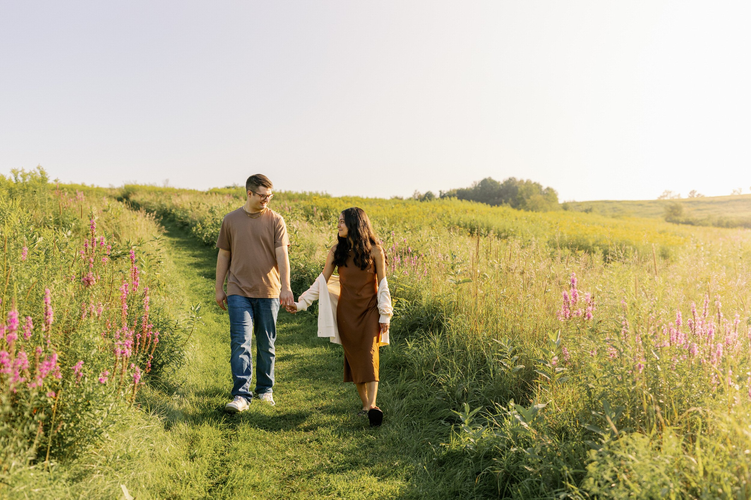 A couple holding hands and walking along a grassy path 