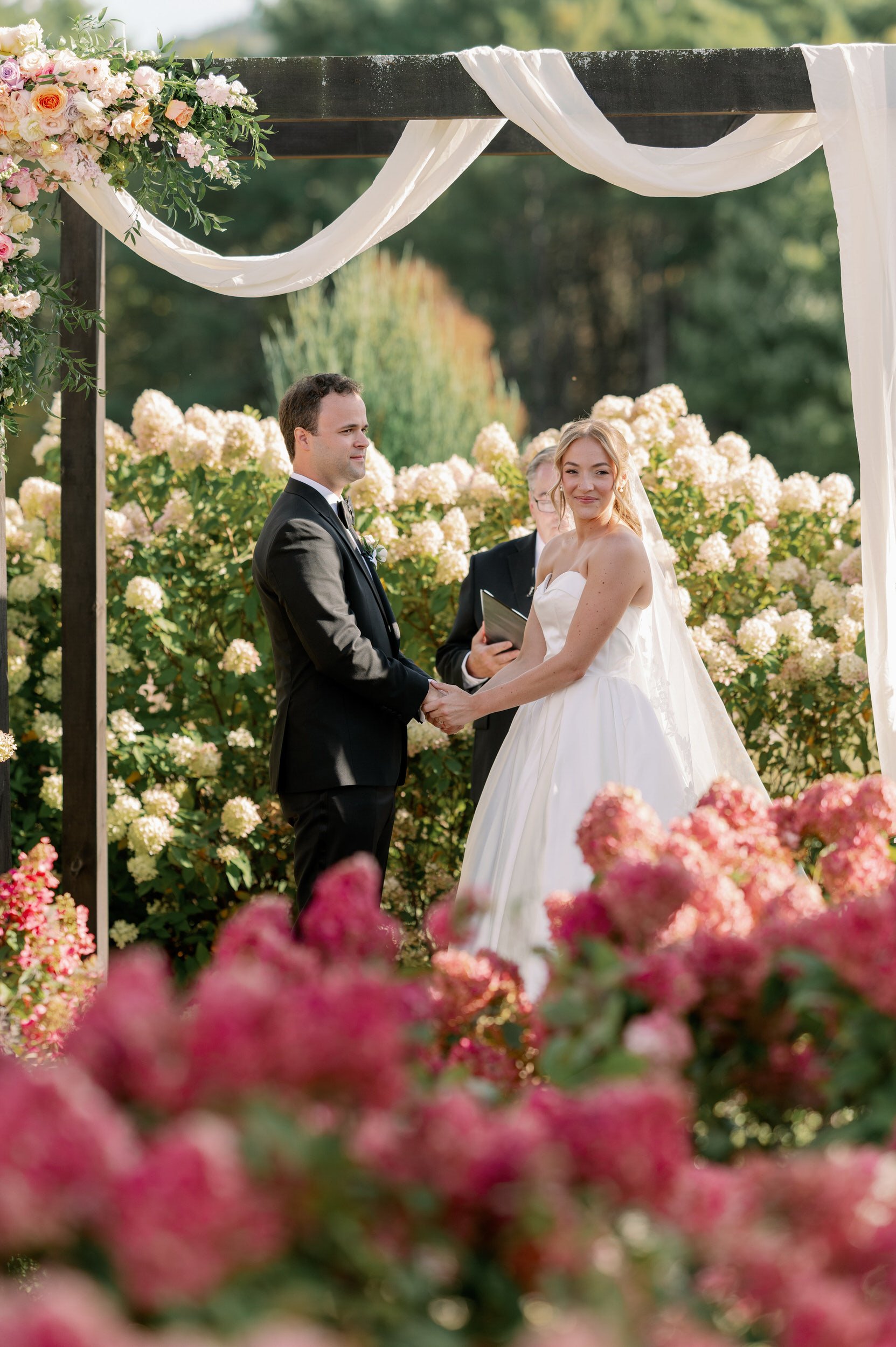 Newlyweds holding hands as one looks out towards their guests during their wedding ceremony