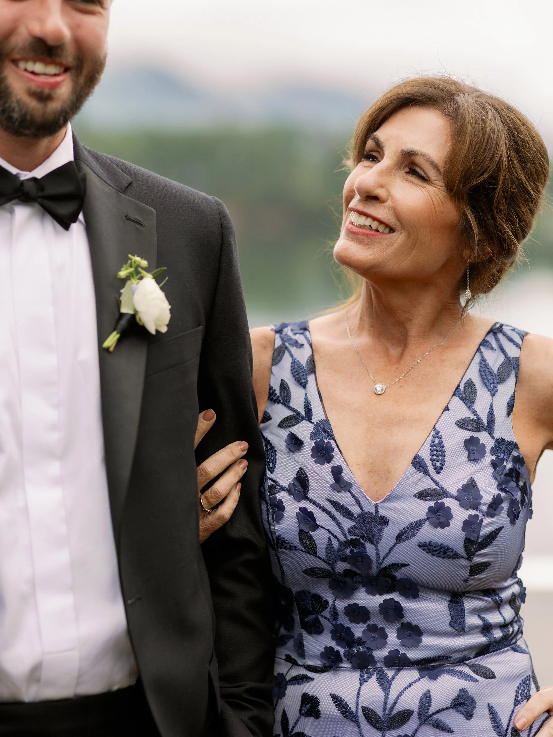 A person in a suit smiling with their parent's arm looped through theirs 