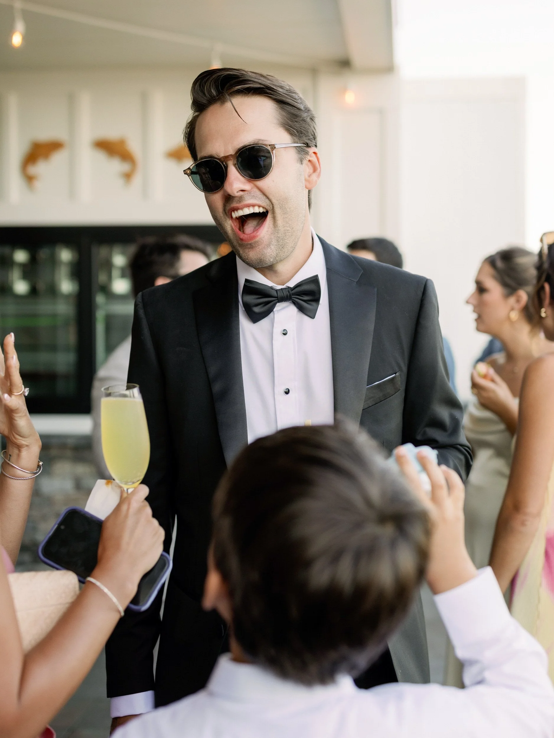 A newlywed in sunglasses laughing and talking with guests 