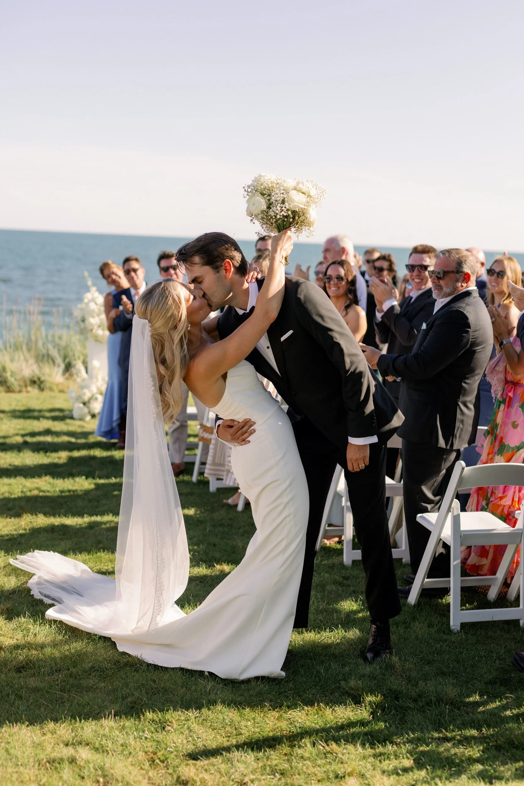  Newlyweds kissing in the middle of the aisle with guests cheering behind them    