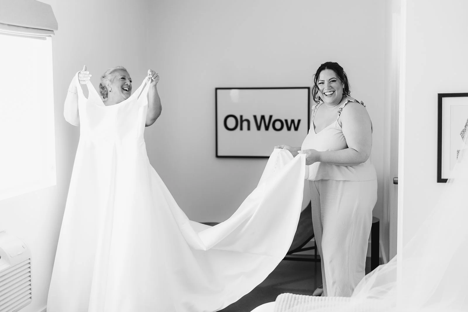 Two people holding up a wedding dress as they smile 