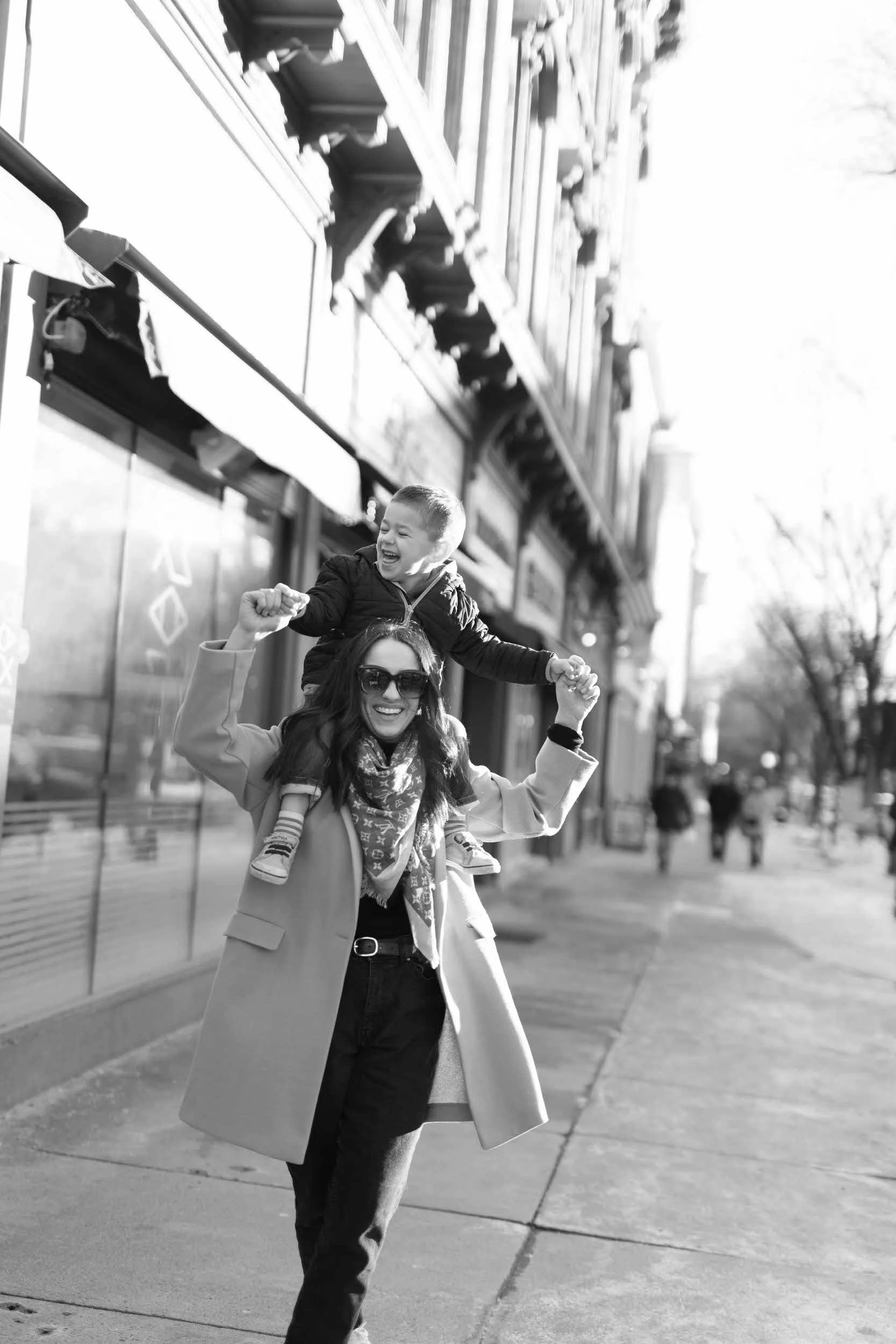 A parent walking down a sidewalk with their child on their shoulders 