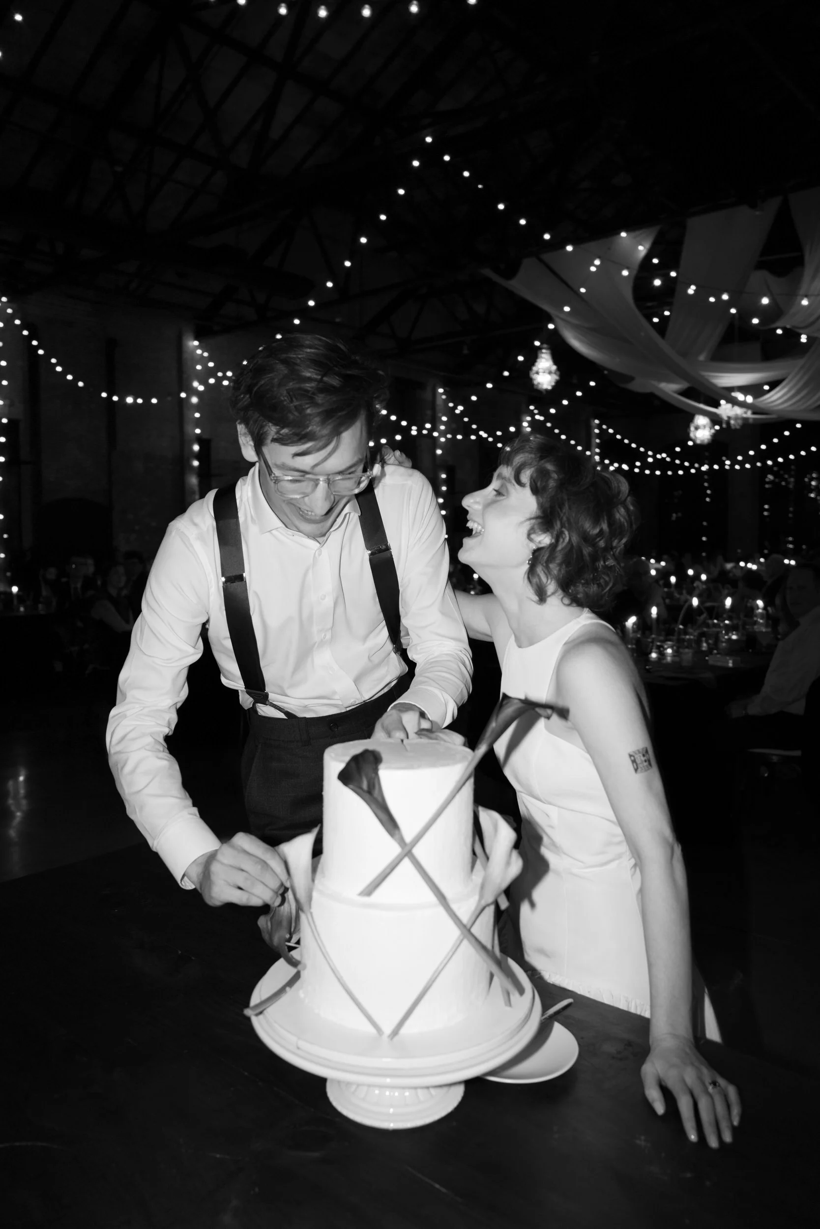 A newlywed couple laughing as they cut their wedding cake 