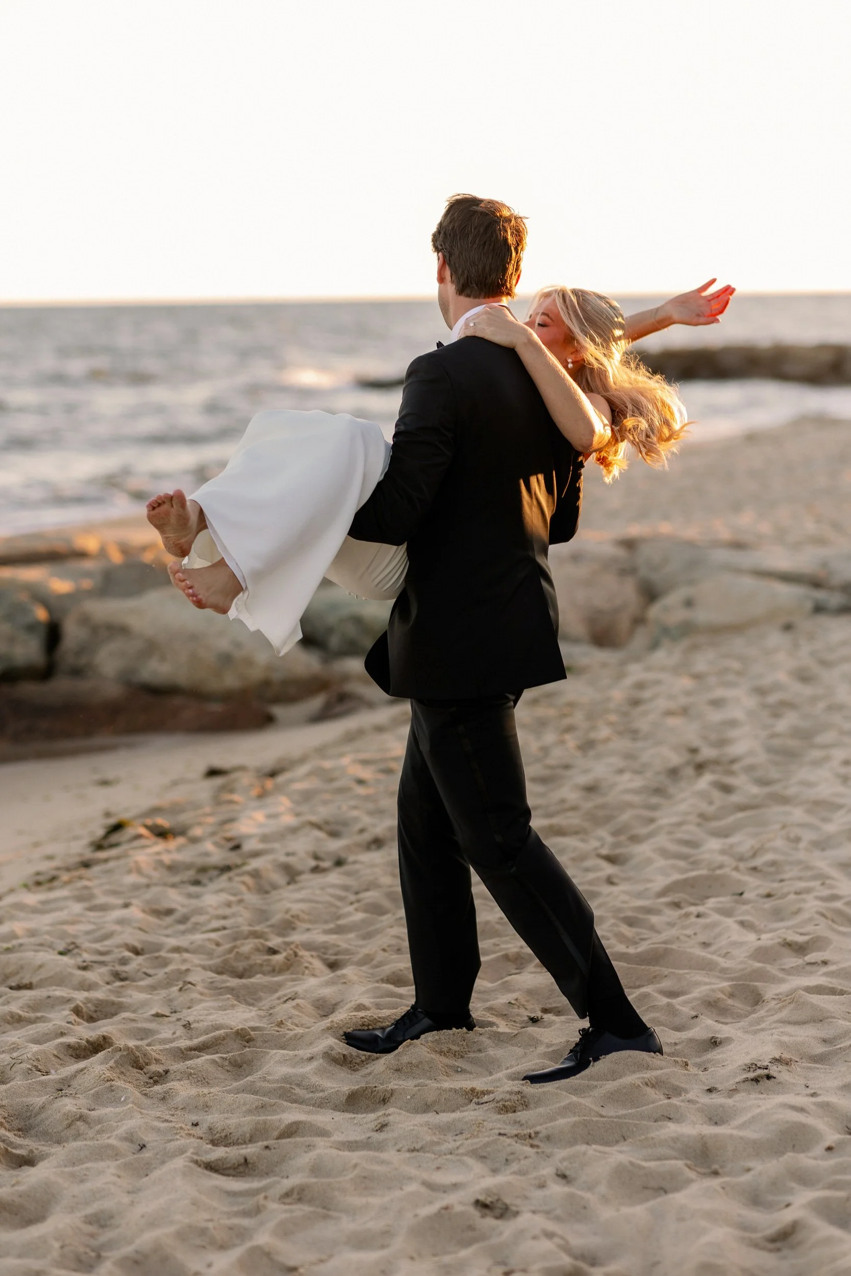 A newlywed holding their partner in their arms and walking on the beach 