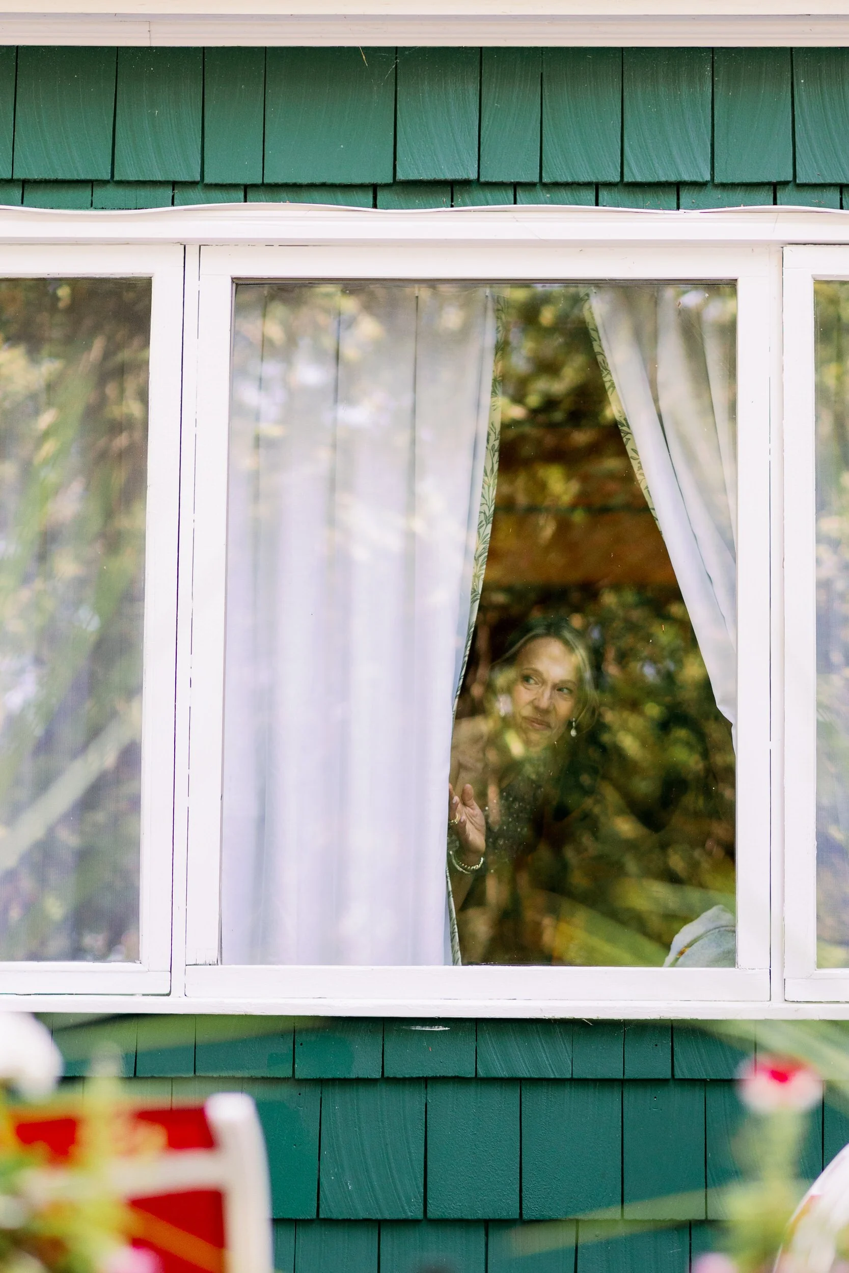 A person peeking out a window from behind a curtain