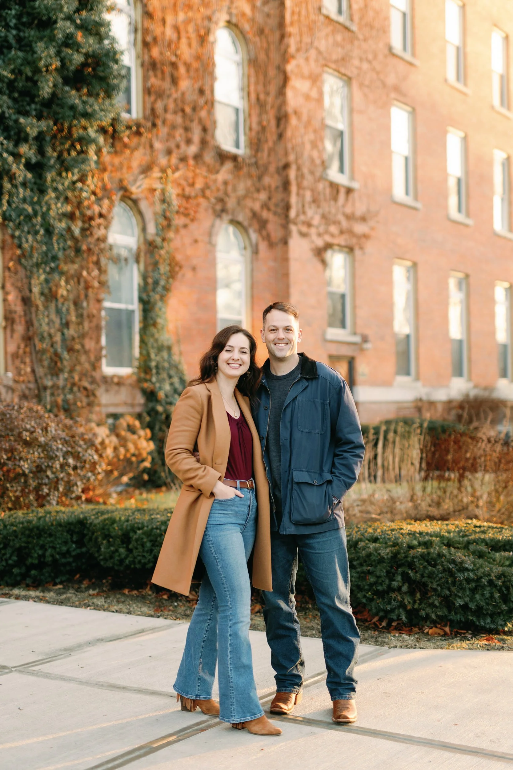 A couple standing next to each other smiling with their hands in their pockets 