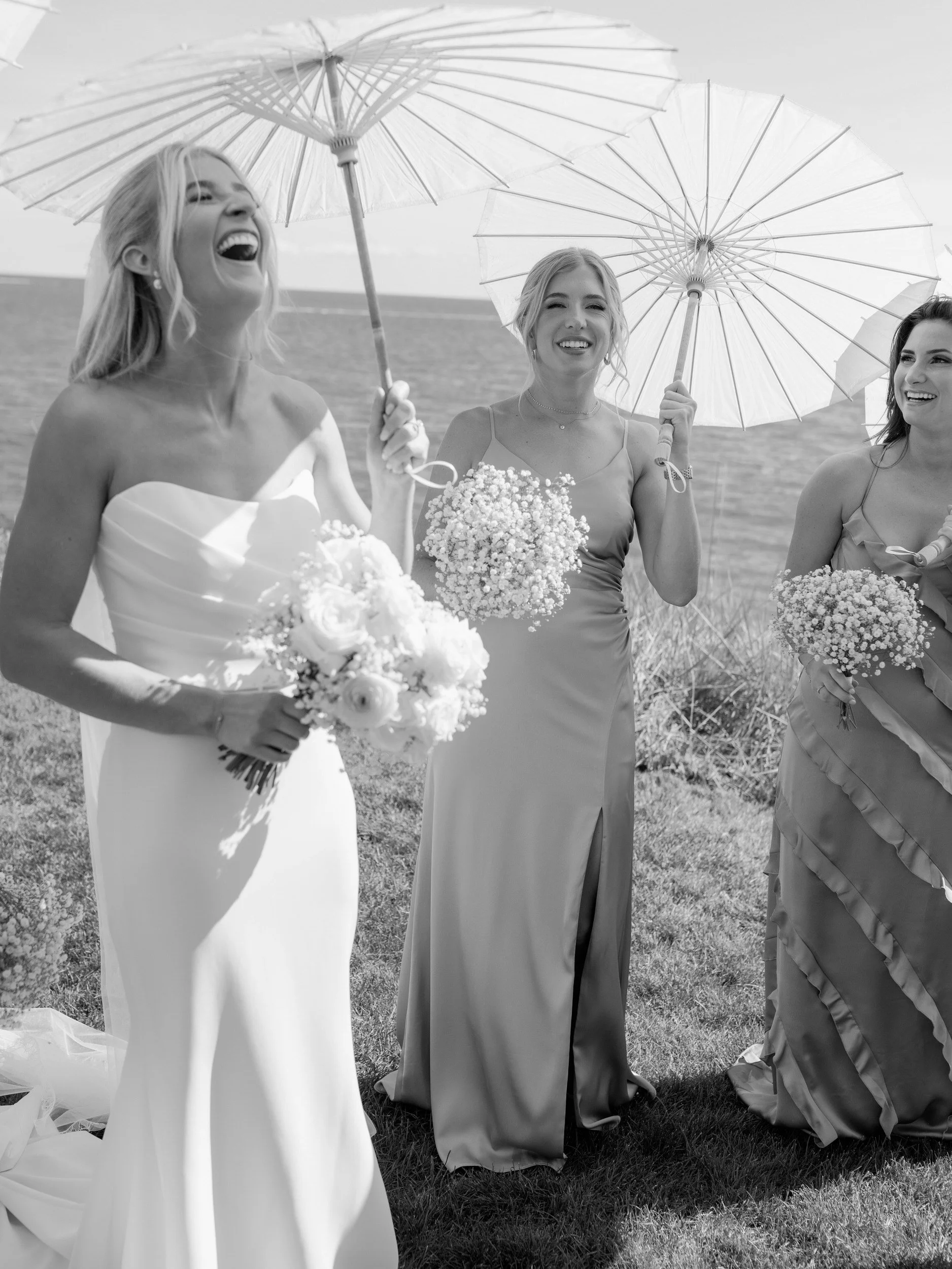 A newlywed laughing with their wedding party while holding decorative umbrellas 
