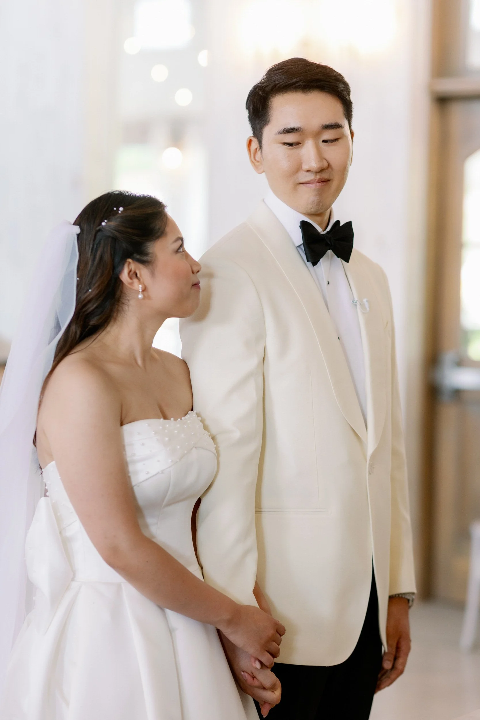 Newlyweds standing side by side as they hold hands and smile at each other 