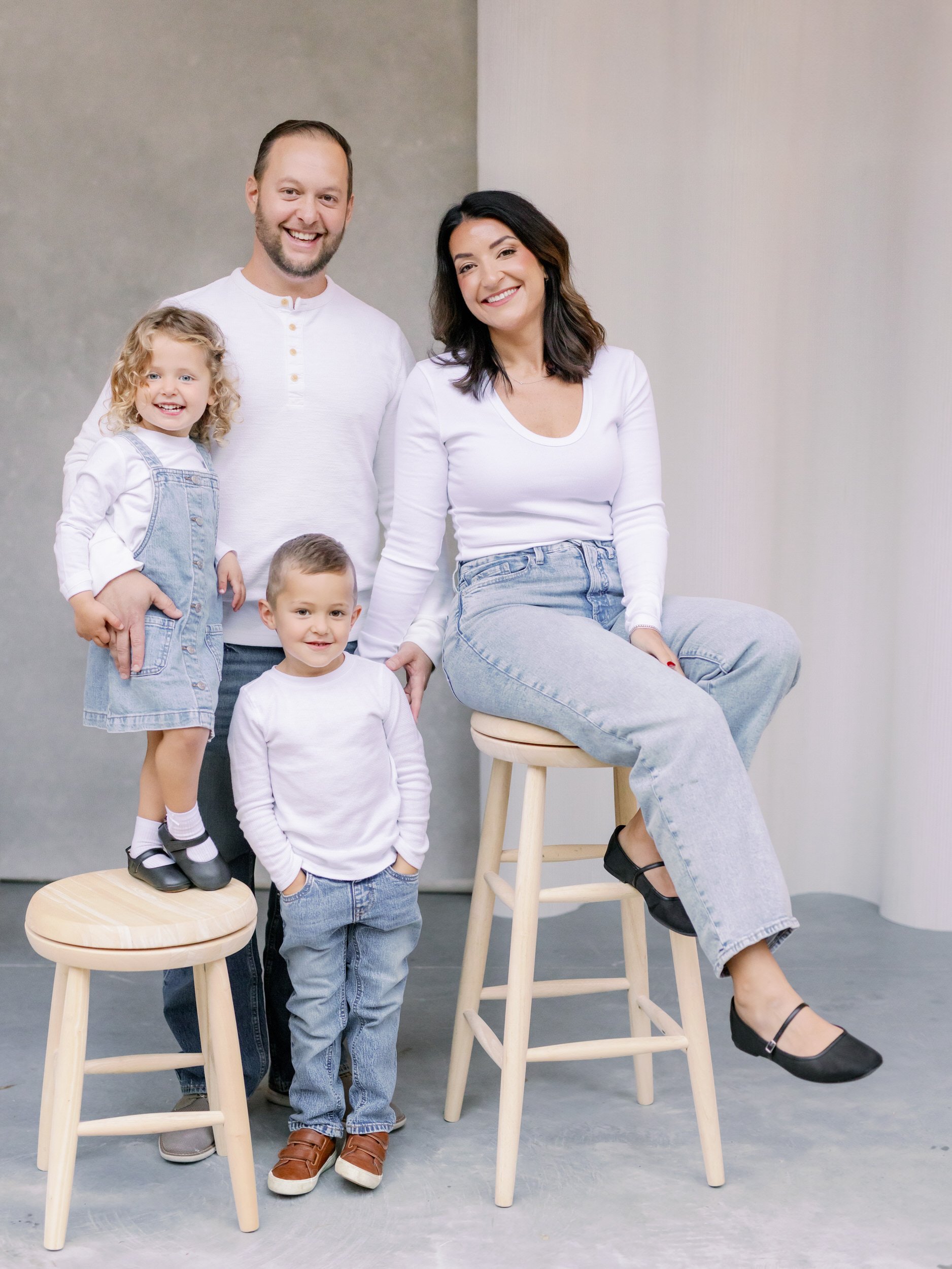 A family of four smiling while sitting or standing next to stools 