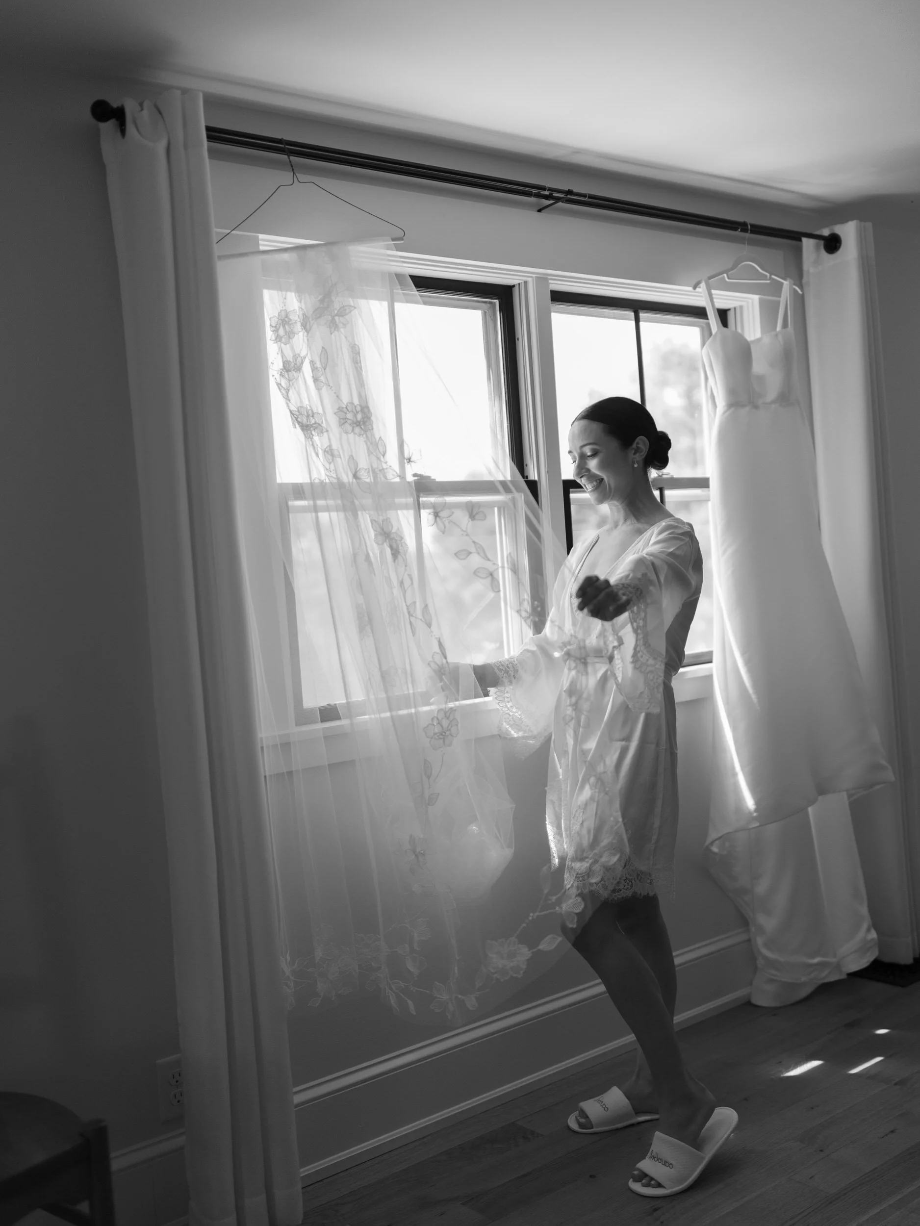 A person looking out a window with a wedding dress hanging behind them 