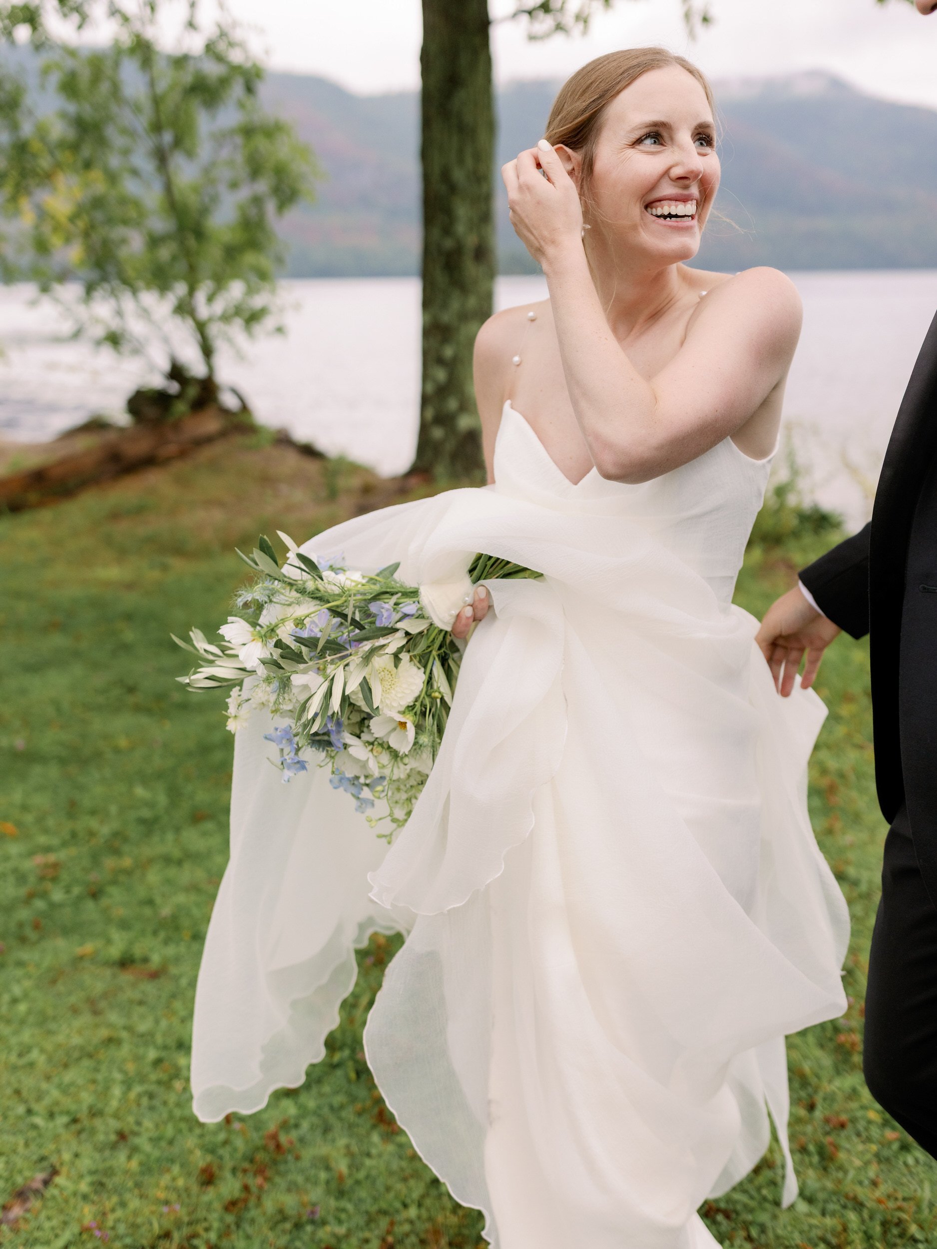 A person in a wedding dress holding a bouquet of flowers and smiling at their partner 