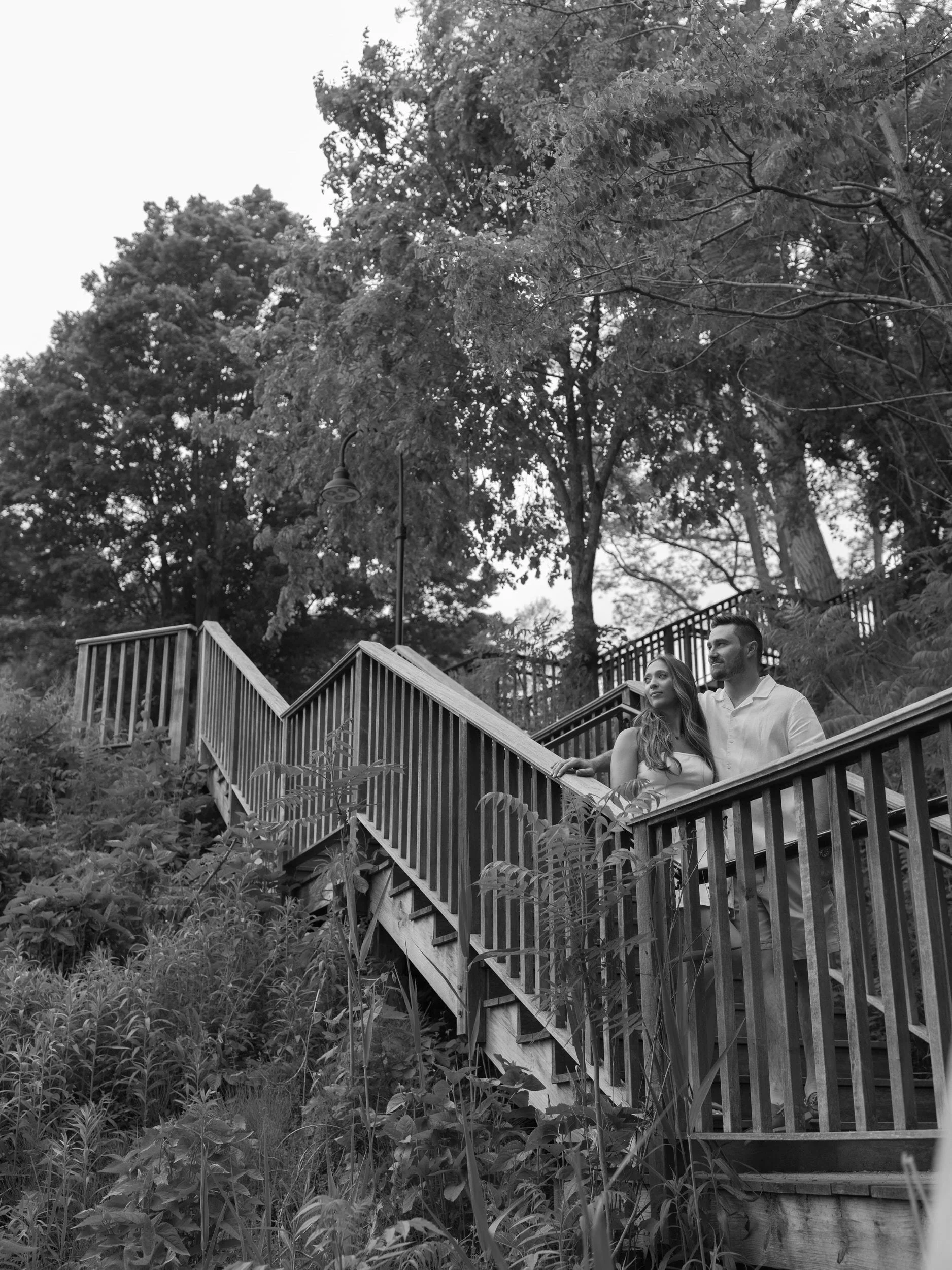 A couple standing on a wooden staircase together looking off into the distance 