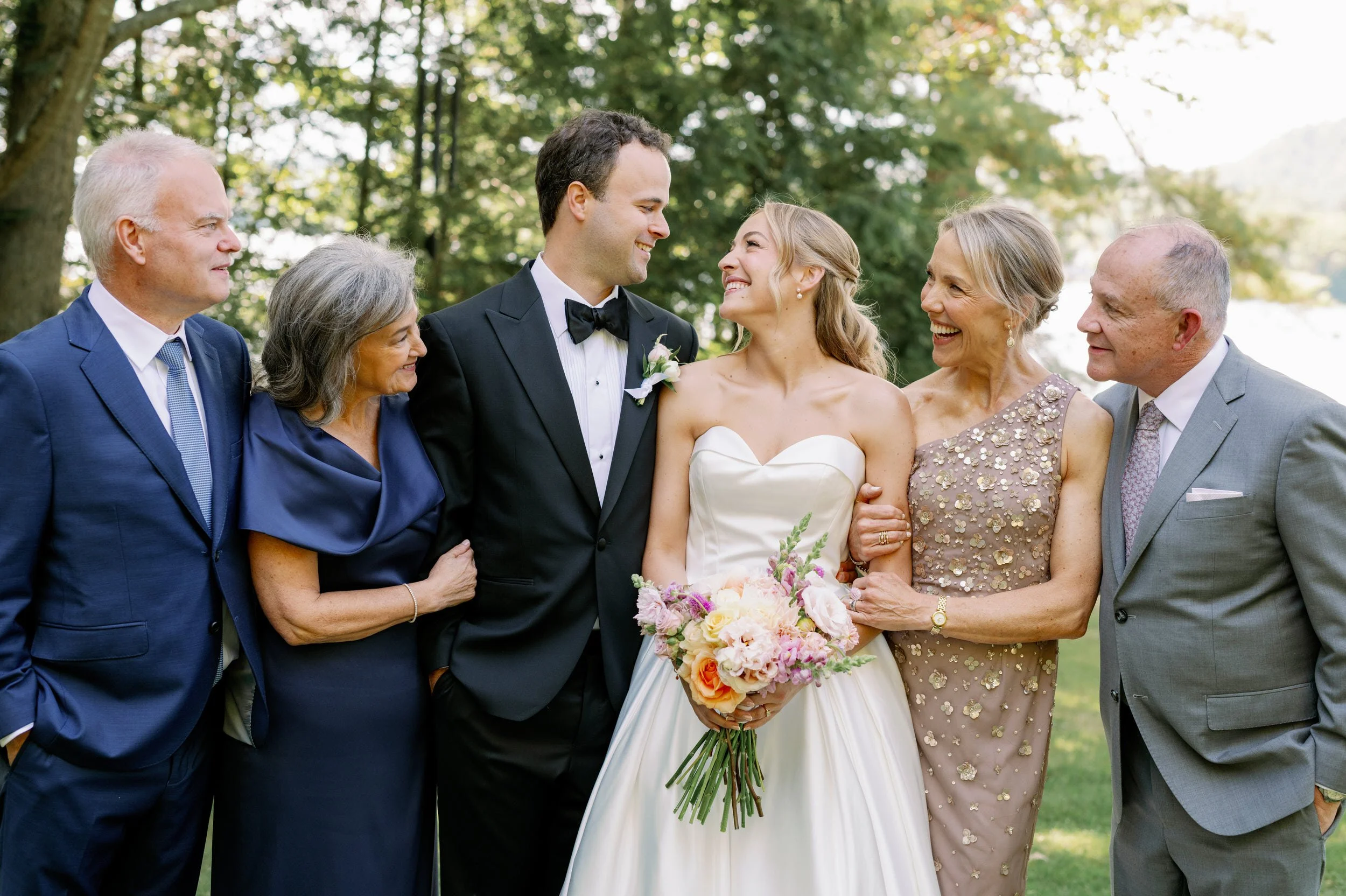 Newlyweds smiling at each other with their parents on either side of them 
