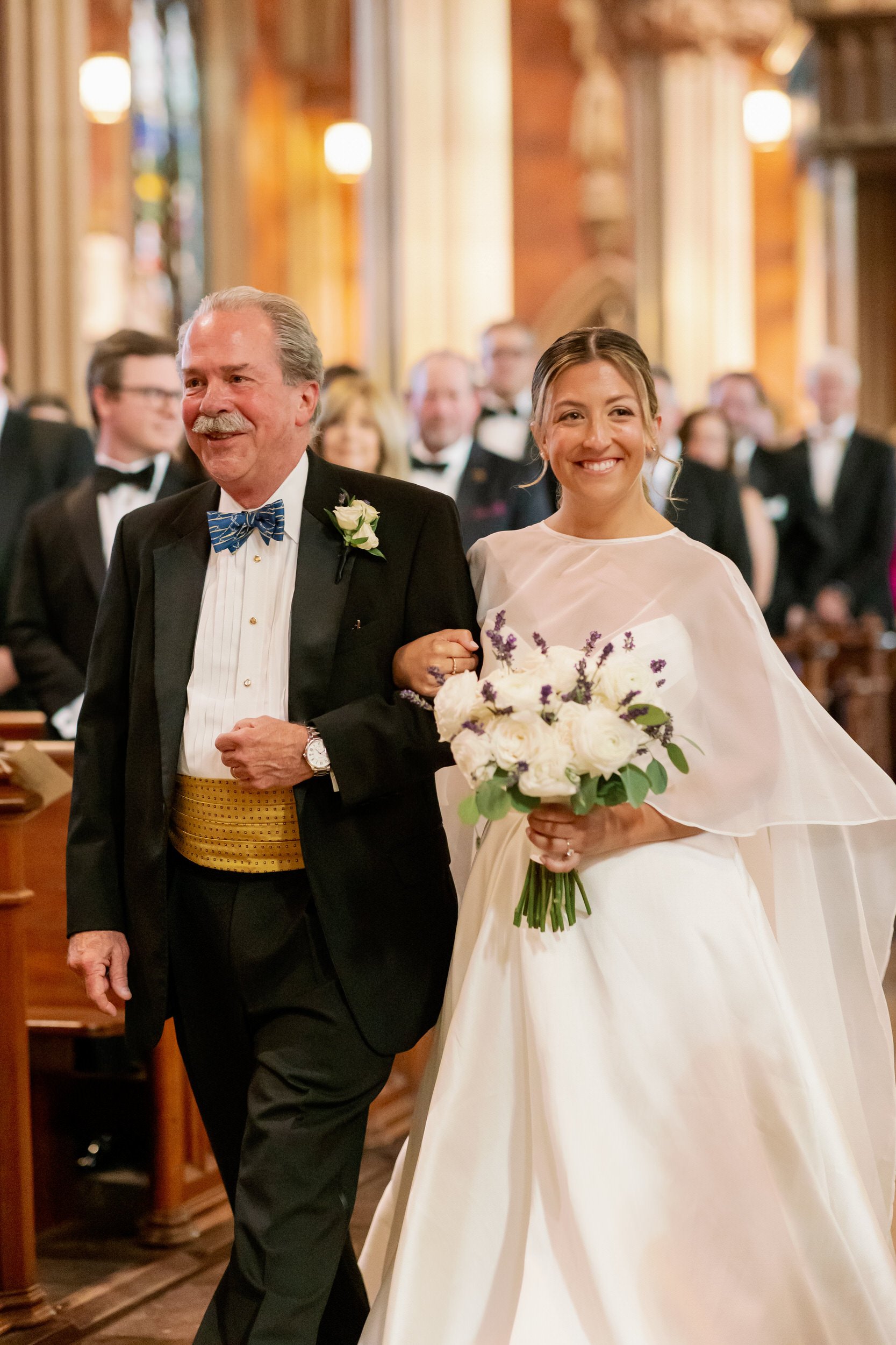 A person in a wedding dress holding a bouquet of flowers and being walked down the aisle 