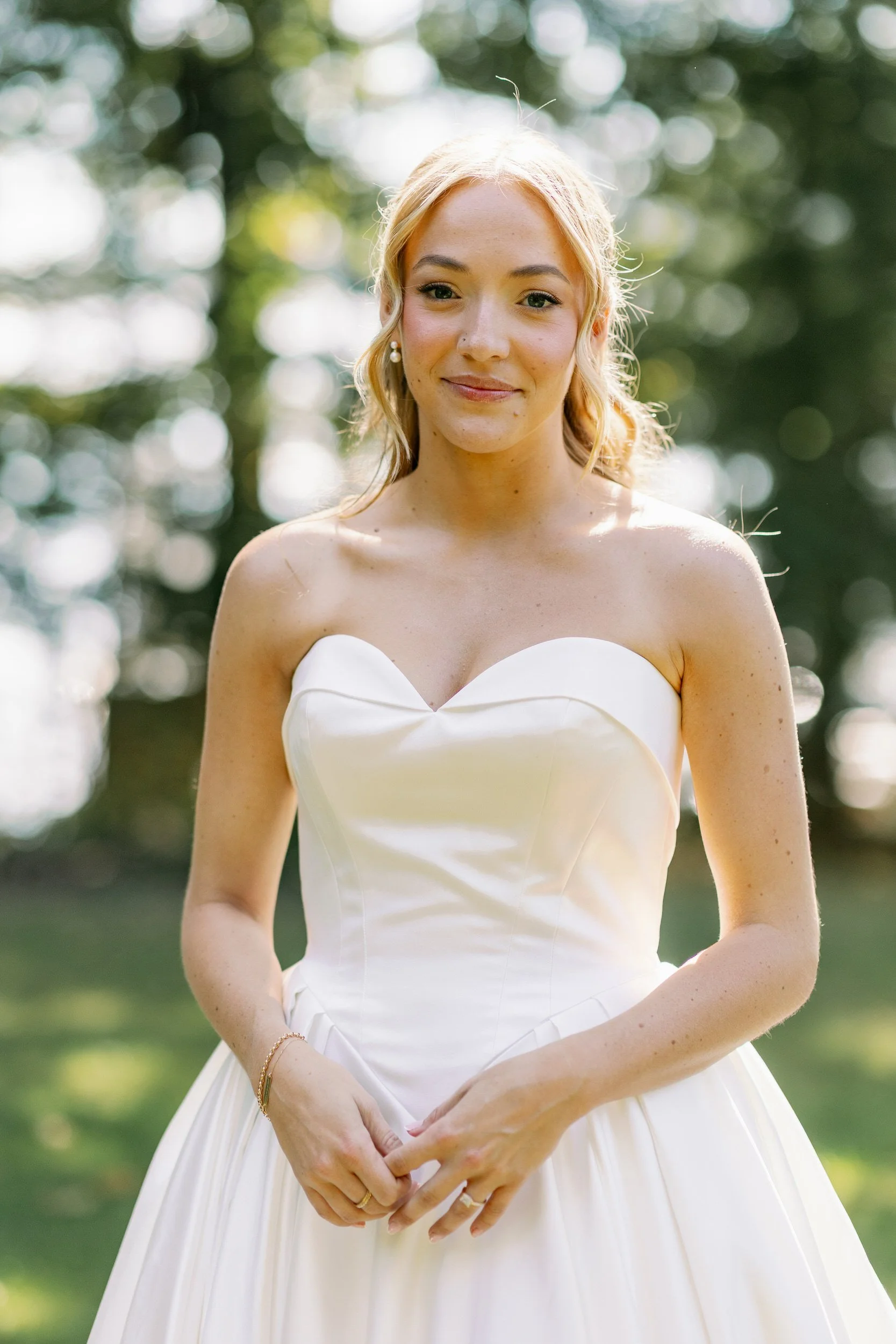 A person in a wedding dress smiling with their hands clasped in front of them 