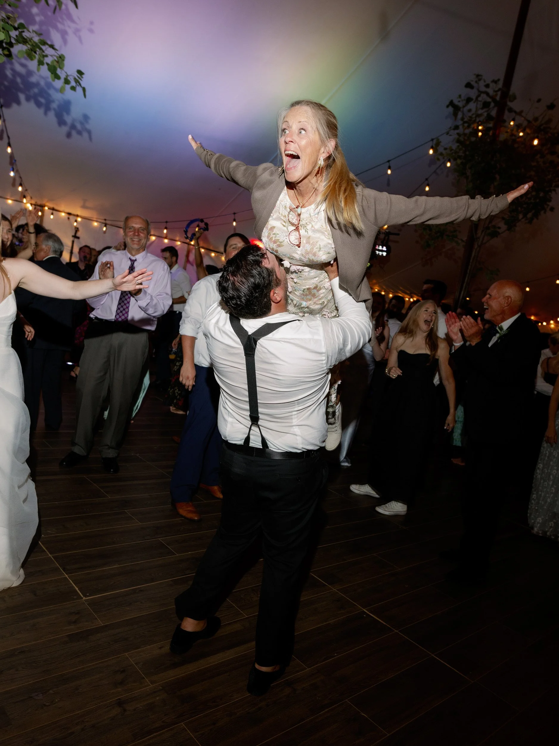 A person lifting someone up as they dance at a wedding reception 