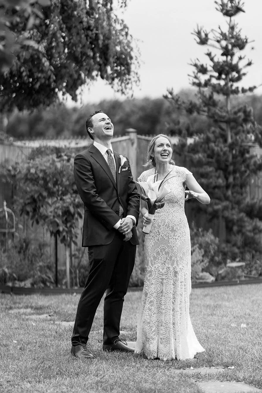 A newlywed couple standing together and laughing as they look up 