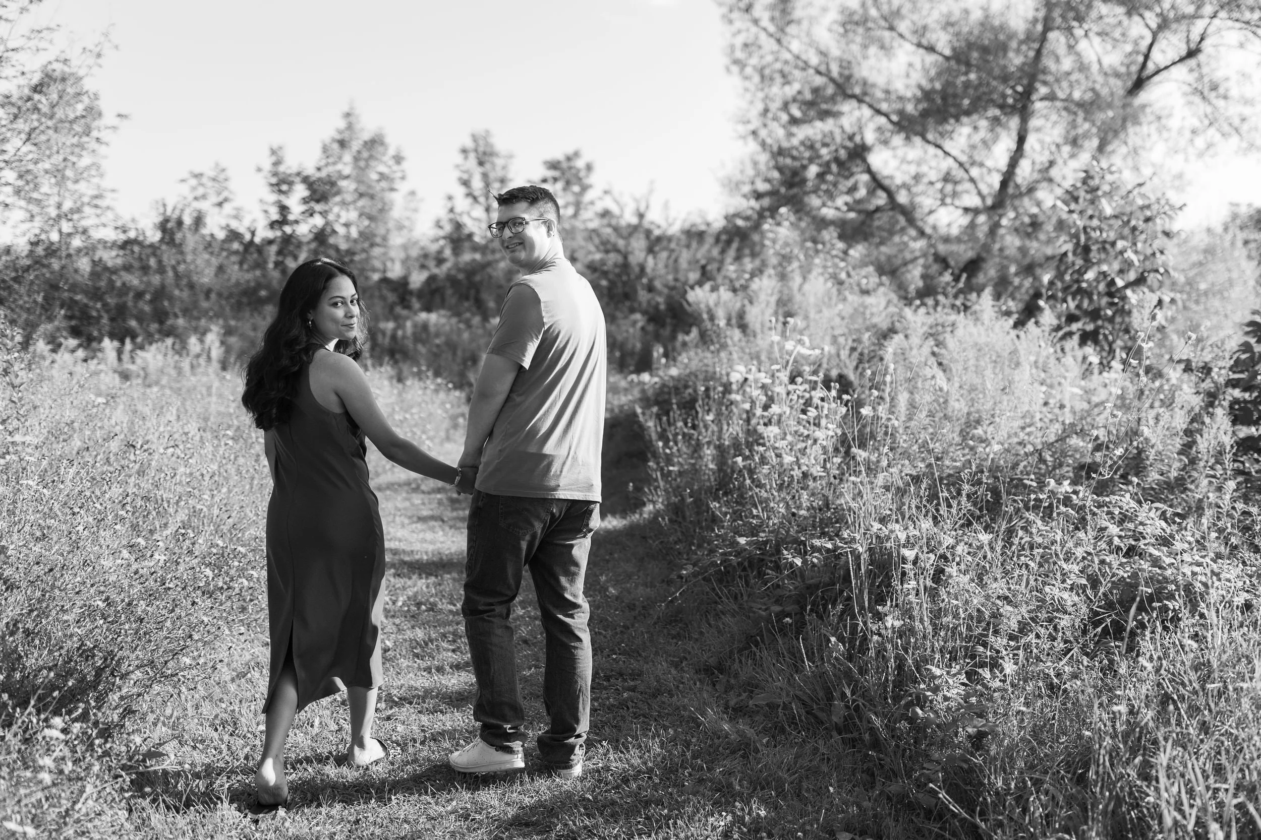 A couple holding hands and walking together as they look back over their shoulders 