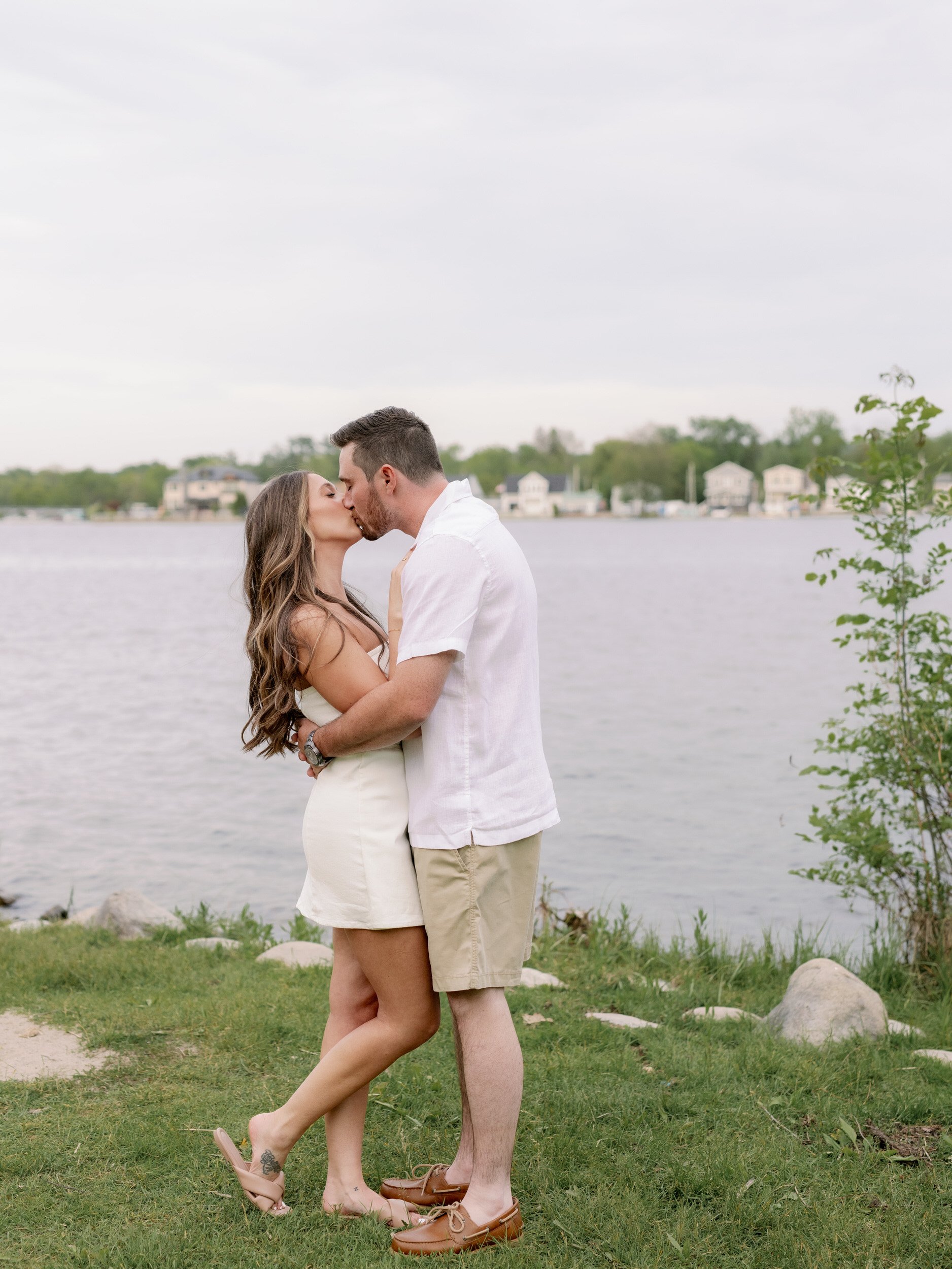 A couple kissing while hugging each other in front of a lake 