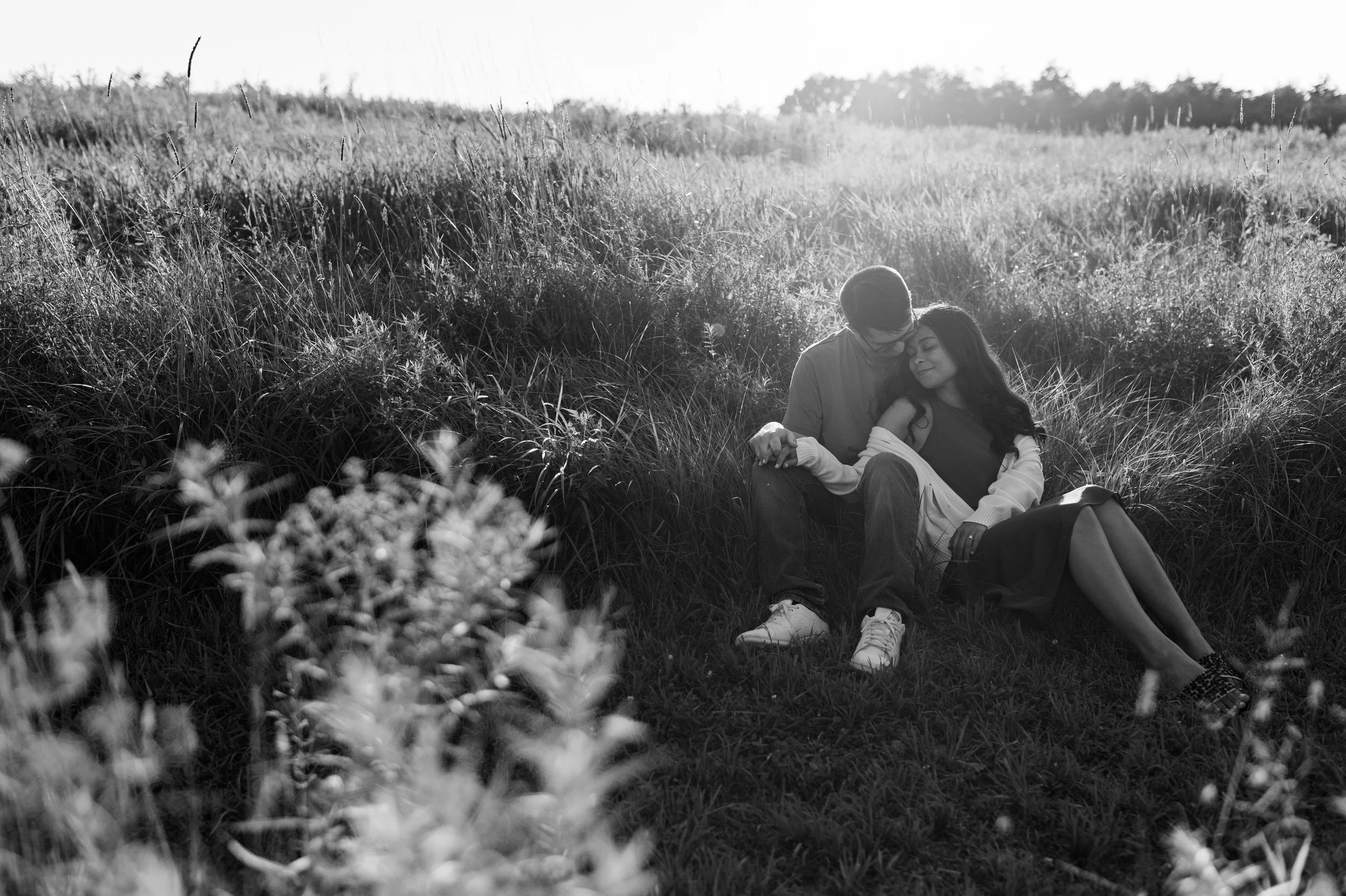 A couple sitting together in a field as one leans into the other 