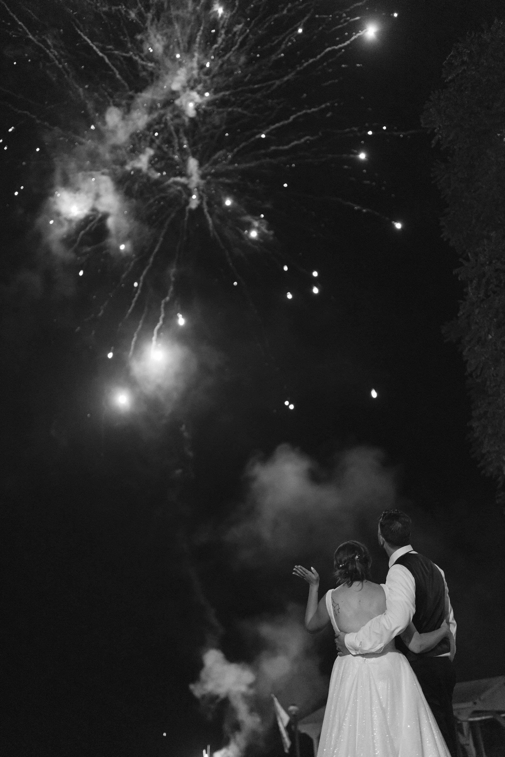A newlywed couple with their arms around each other watching fireworks
