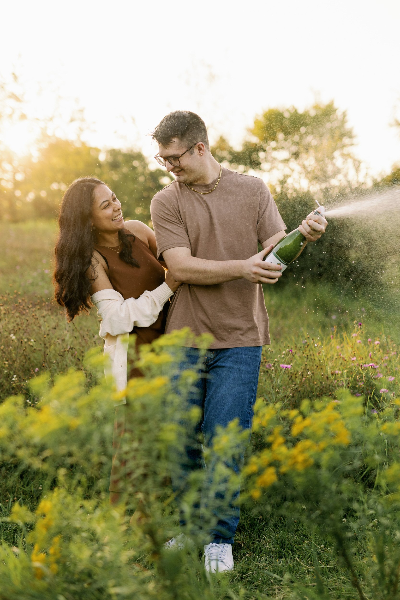 A couple laughing as they pop a bottle of champagne 
