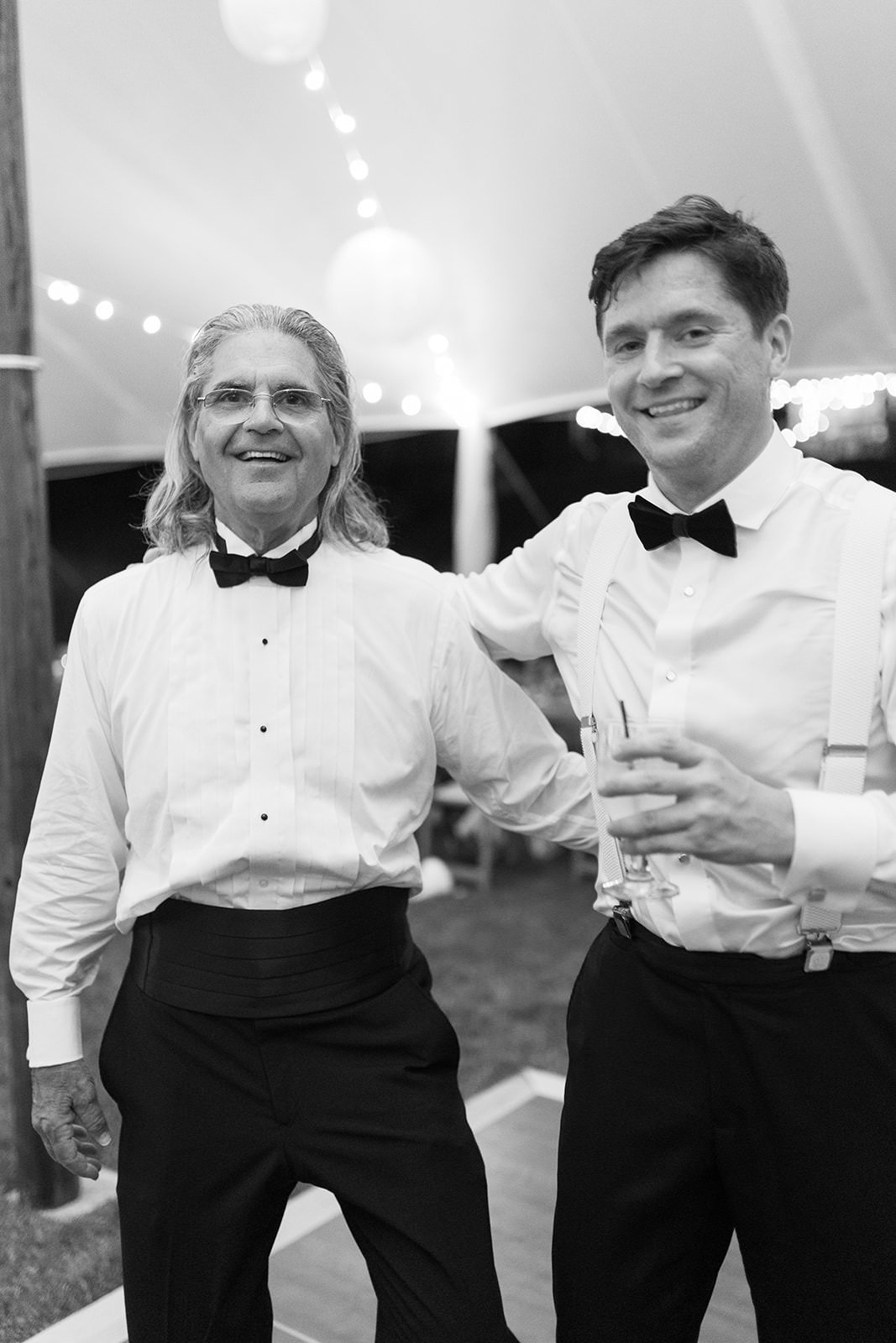 Wedding guests in suits with their arms around each other laughing 