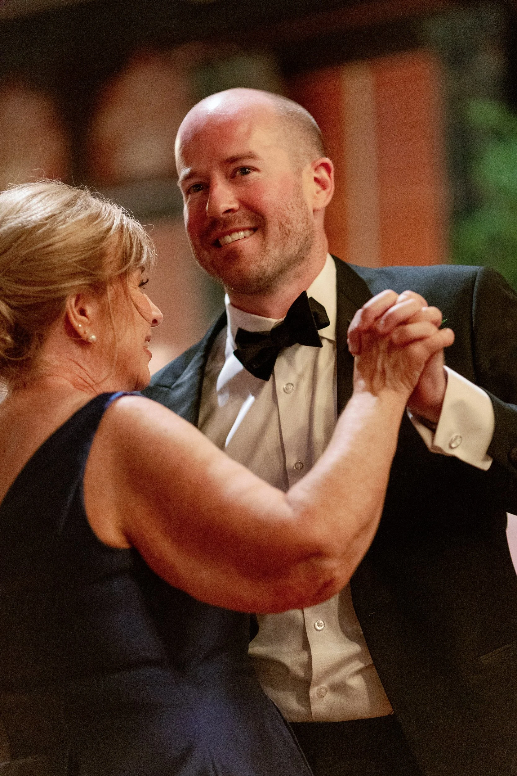 A newlywed smiling and dancing with their parent at their wedding 