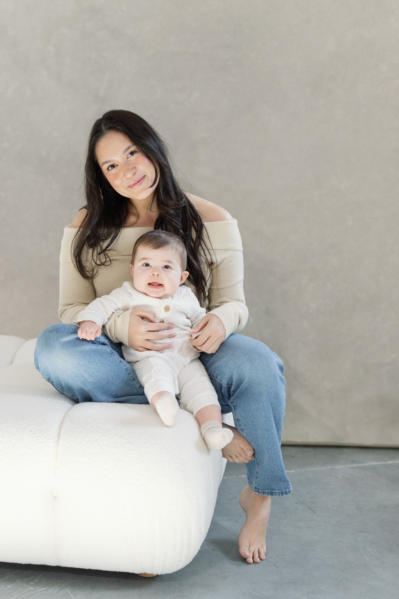 A parent sitting on a small couch with their newborn in front of them 

