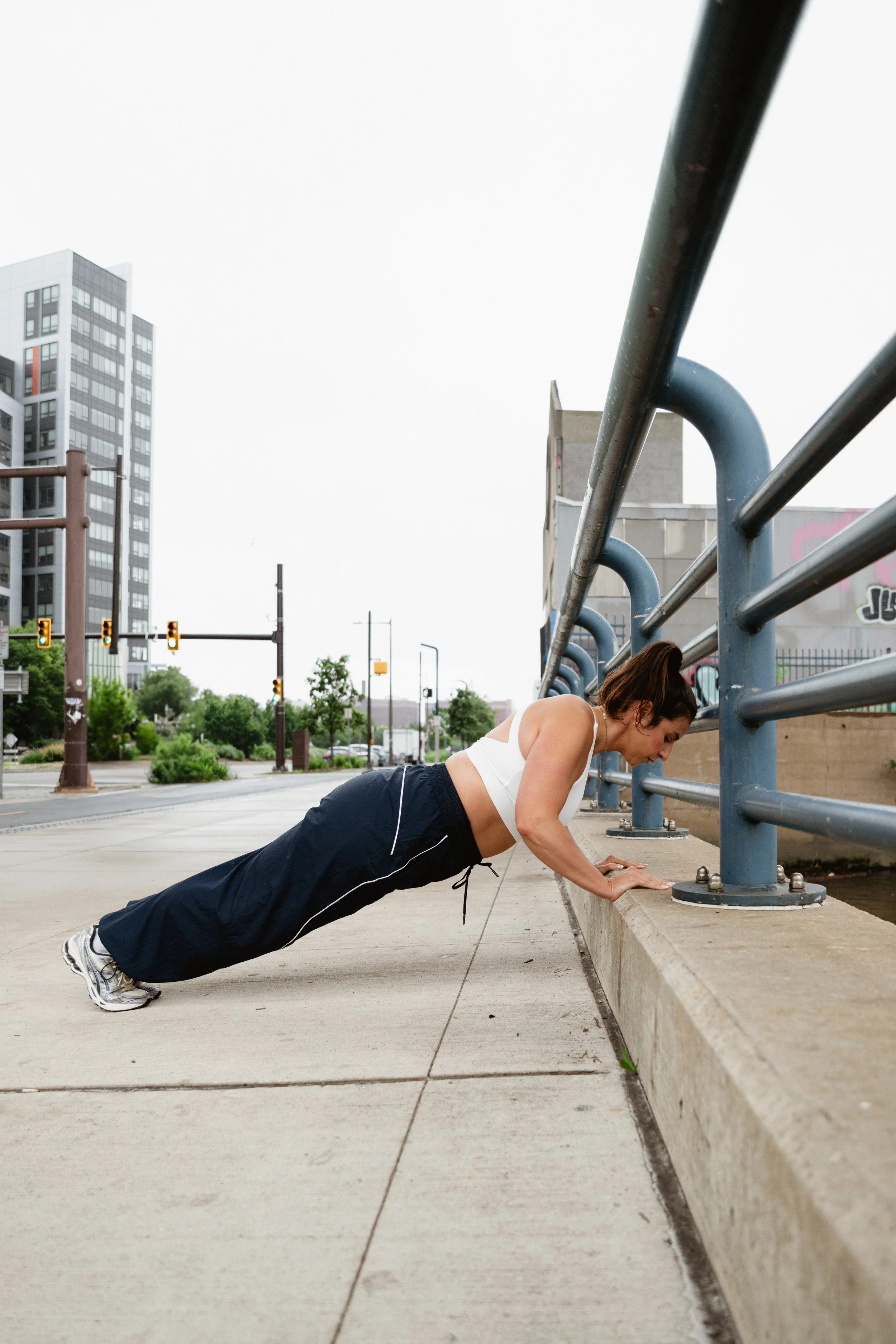 Woman raising her body in push up position on sidewalk railing.