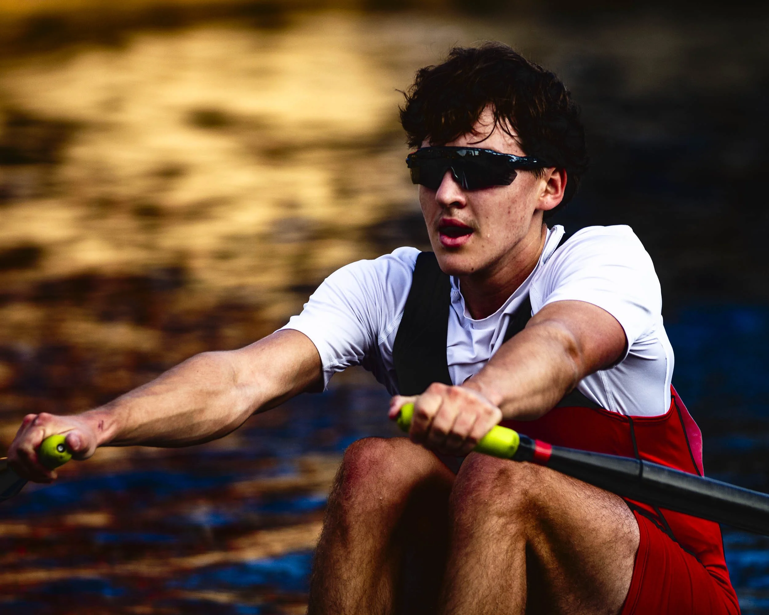 Young man paddling a kayak on water at sunset, wearing sunglasses and athletic clothing.