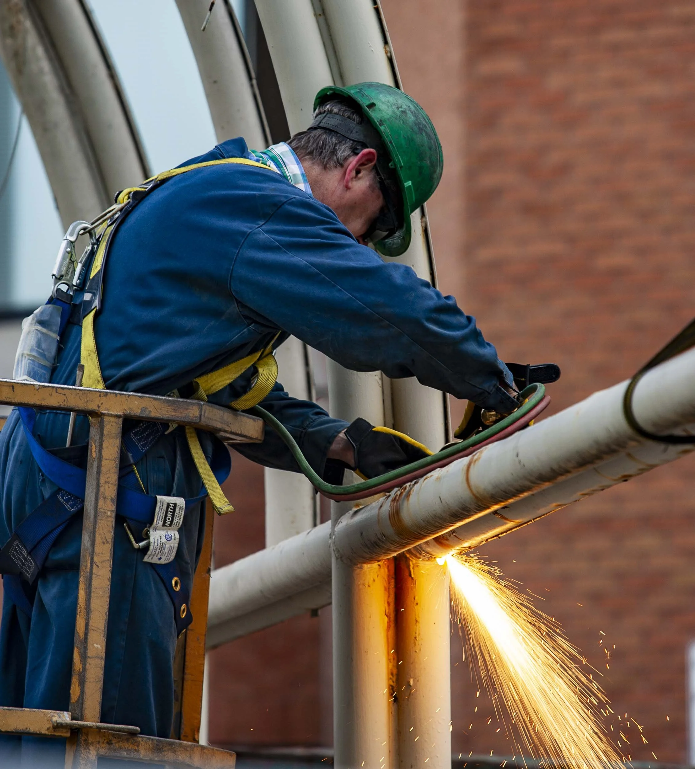 A worker welding metal pipes on a scaffold, with sparks flying from the welding process.