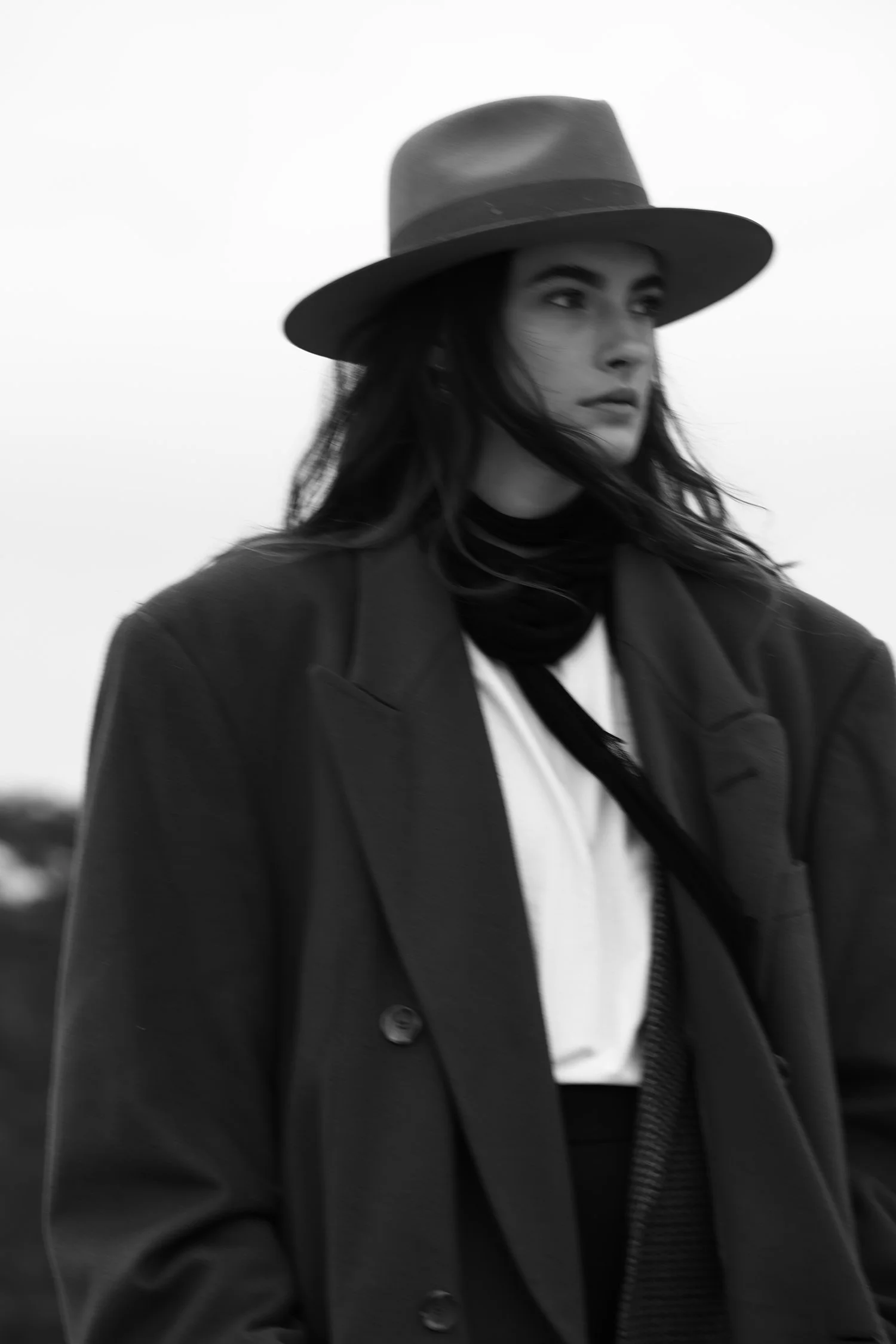 Black and white photograph of a woman wearing a wide-brimmed hat and coat, standing outdoors.