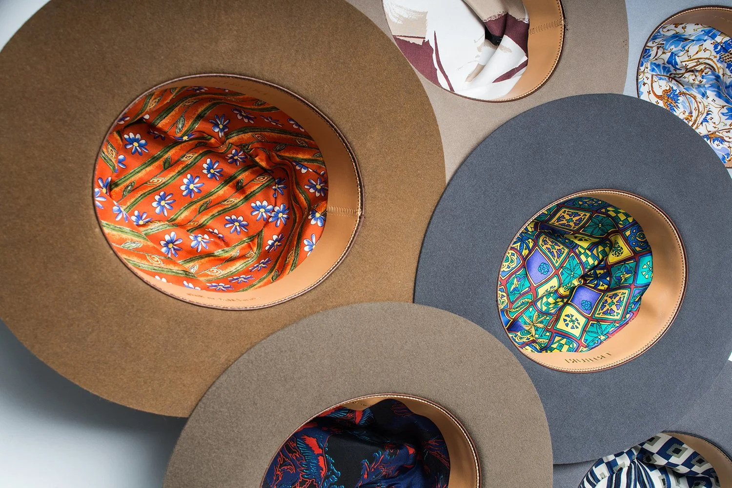 A collection of wide-brimmed hats with colorful, patterned interiors visible through the openings.