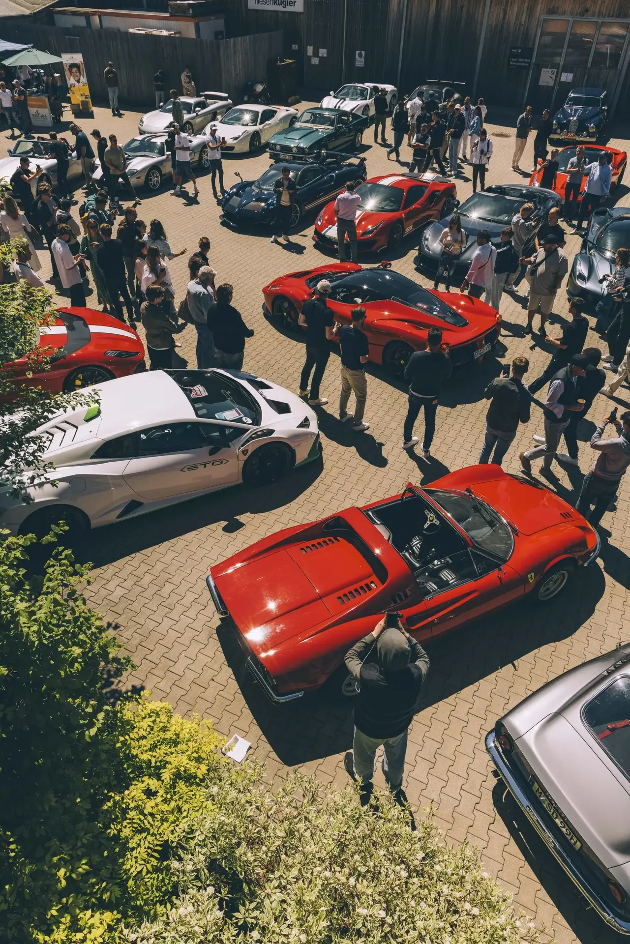 Outdoor car show featuring various luxury and sports cars, with people walking around and taking photos.