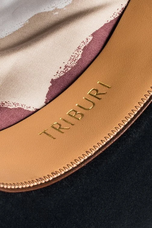 Close-up of a designer handbag with the brand name 'TRIBUR' embossed in gold on tan leather, with fabric lining visible inside.