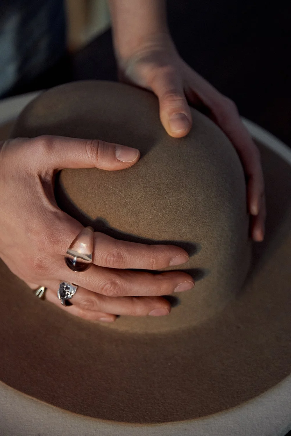Hands shaping a felt hat on a wooden hat block during the hat-making process.