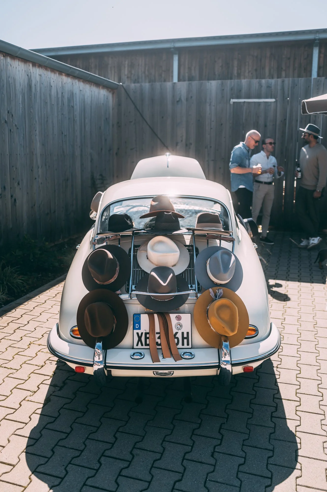 Classic white vintage car parked on brick pavement with hats displayed on a rack at the back.