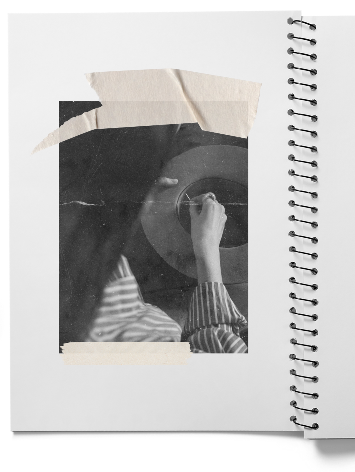 Black and white photo of a person's hand drawing on a notebook page, seen from above, with torn tape pieces attached to the page.