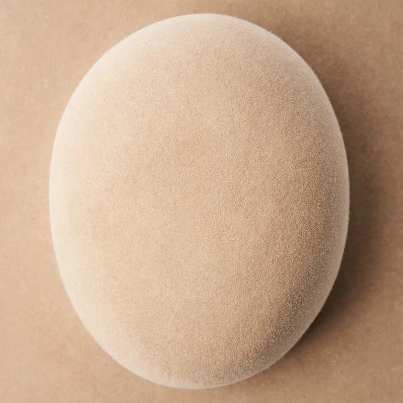 Unshaped beige felt hat with open crown resting on a neutral background.