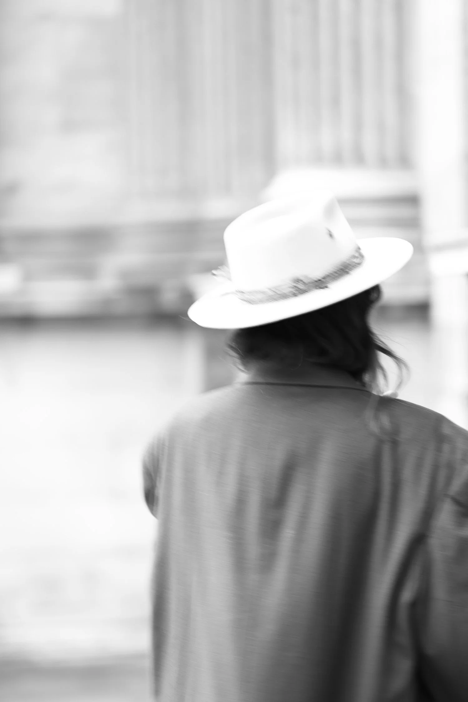 Person wearing a hat and coat, seen from behind while walking outdoors.