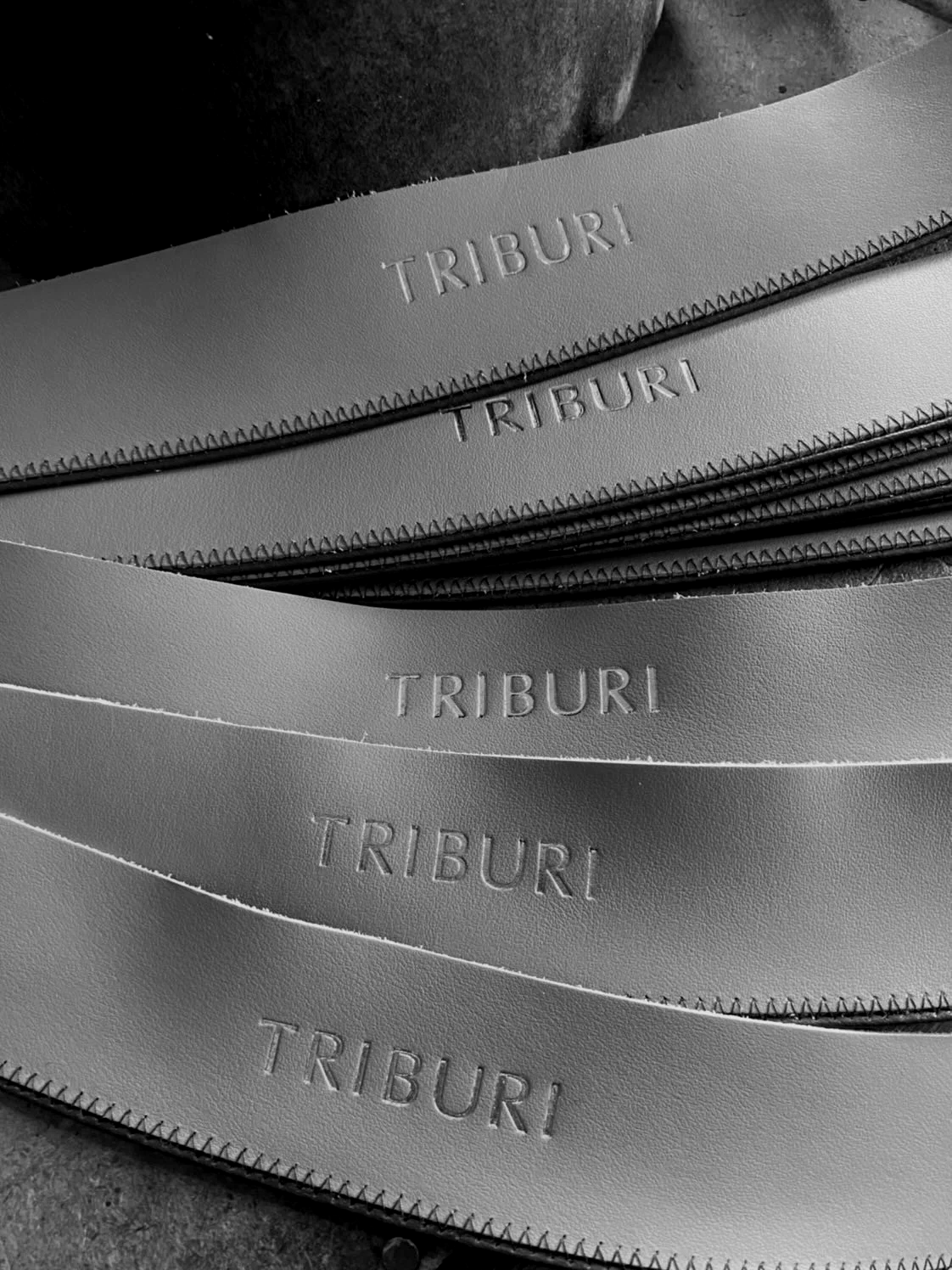 Multiple leather belts with the brand name "TRIBURI" embossed on them, arranged overlapping each other.