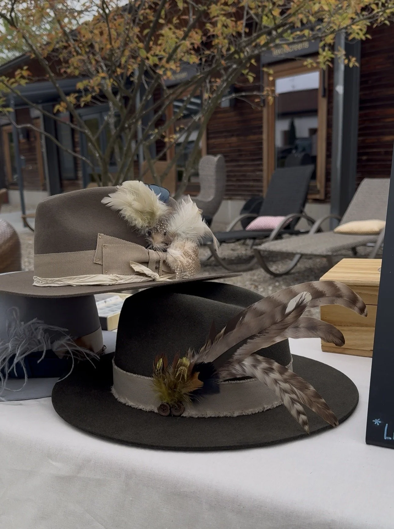 Two handcrafted hats decorated with feathers, displayed on a table in a hat studio.