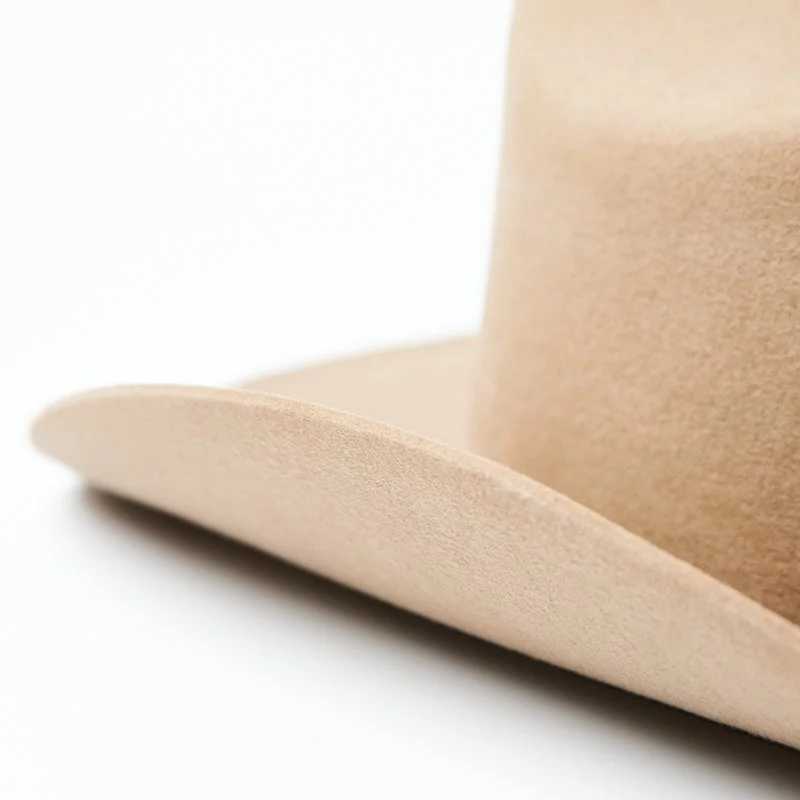 Curved brim detail of a beige felt hat on a white background.