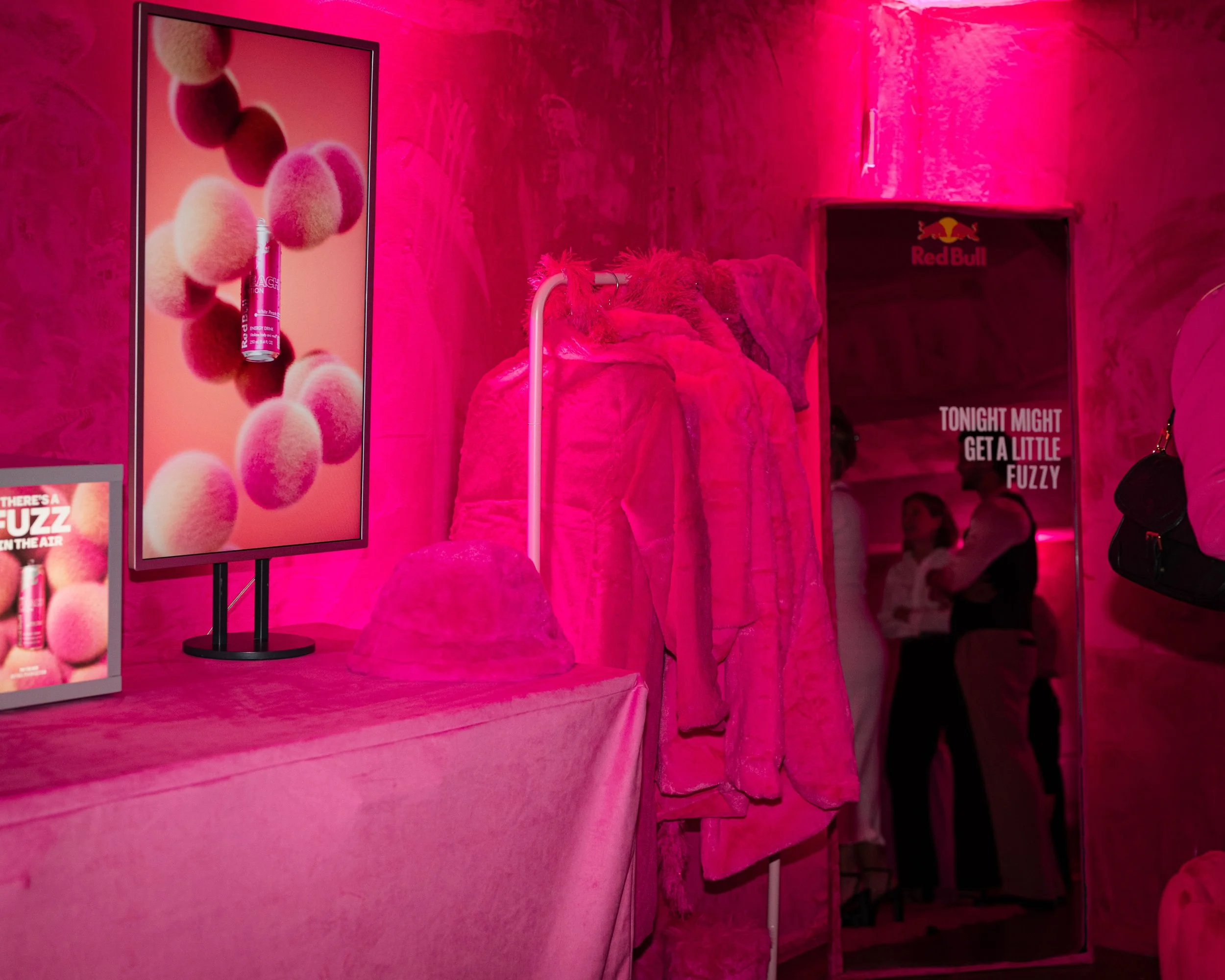 Red Bull Peach Edition pop-up experience bathed in bright pink light, featuring fuzzy pink décor, faux-fur coats and product displays.
