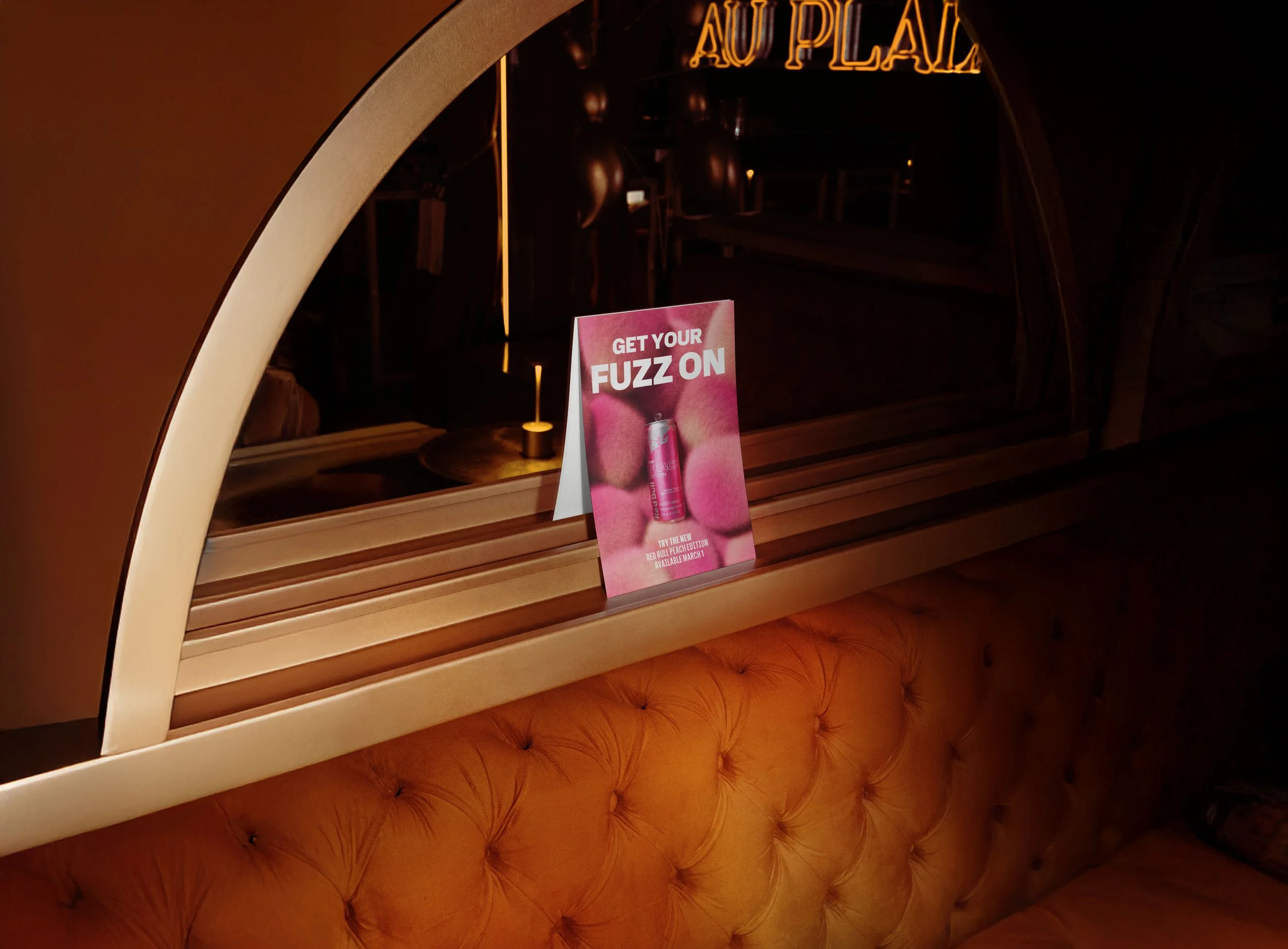 Red Bull Peach Edition ‘Get Your Fuzz On’ tabletop ad displayed in a warmly lit bar booth, featuring a pink can against a fuzzy pink background.