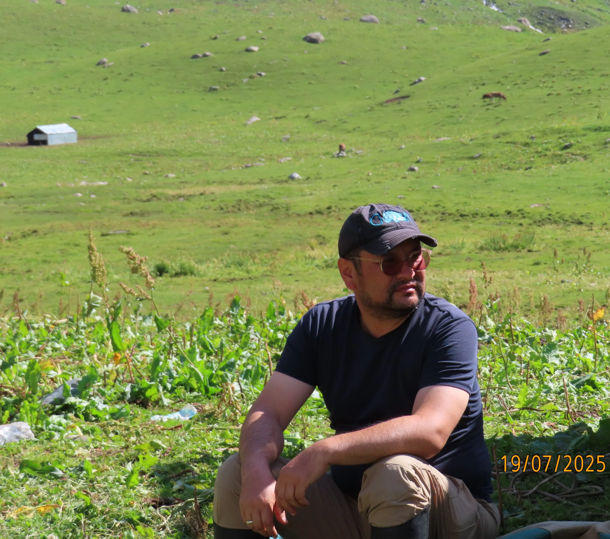 Munarbek Kuldanbaev sits in a green mountain pasture
